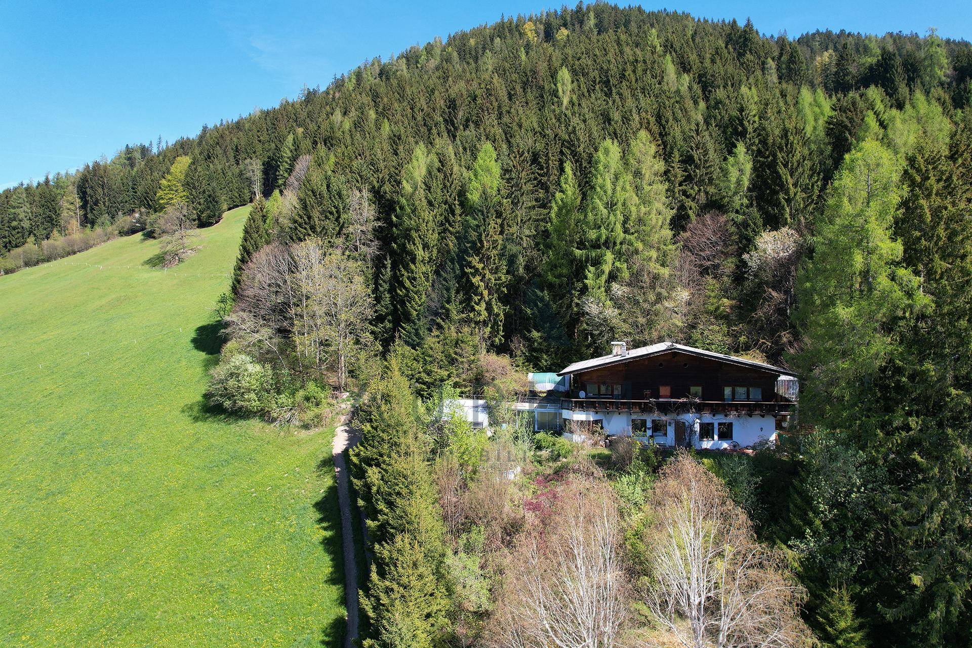 Holzchalet am Hang, umgeben von Wald und Wiesen, mit weitem Blick ins Tal.
