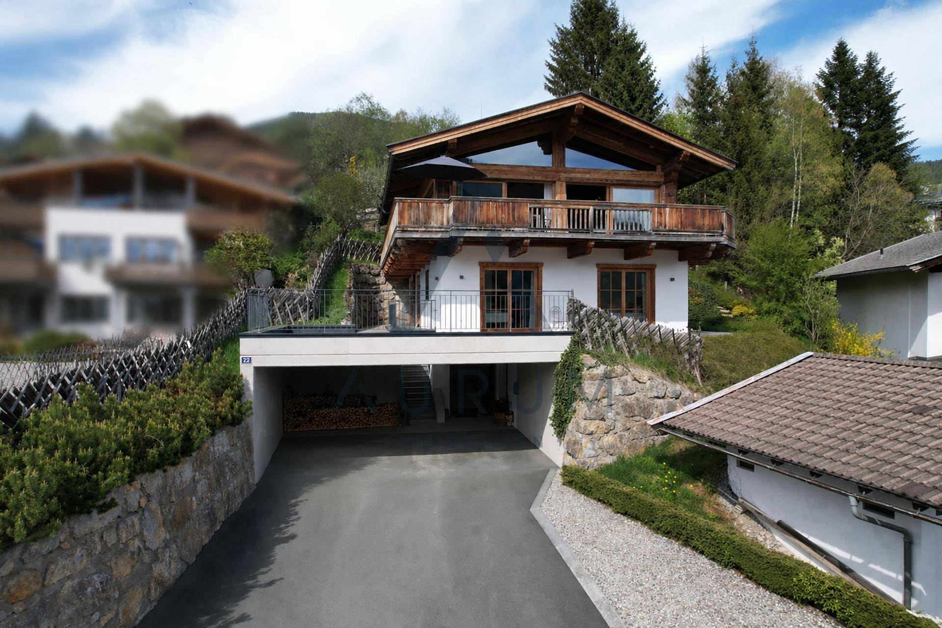 Chalet mit Zufahrt zur Tiefgarage und umgebender Steinmauer in alpiner Umgebung.