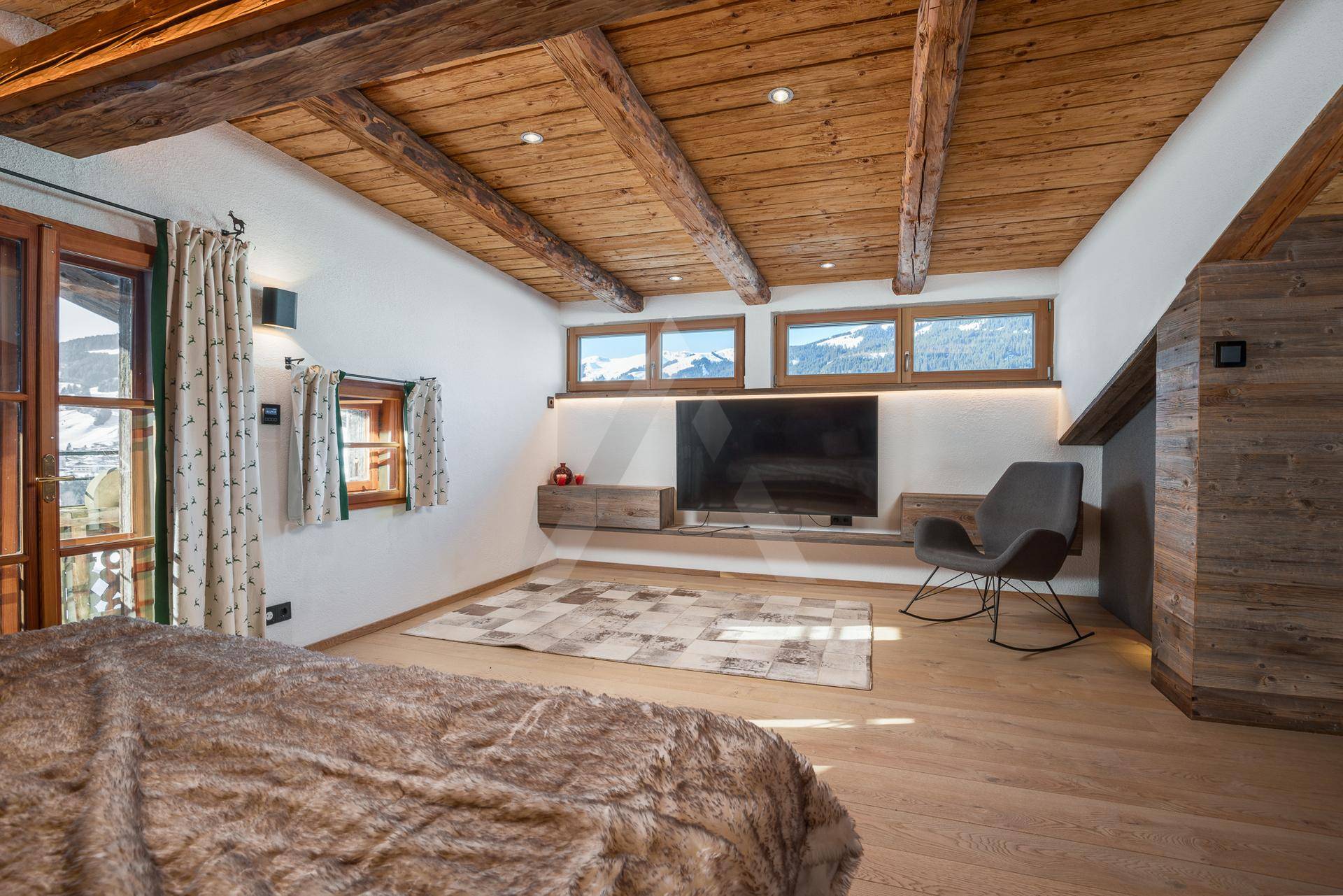 Schlafzimmer mit Holzbalken, Holzboden und Bergblick durch die Fenster.