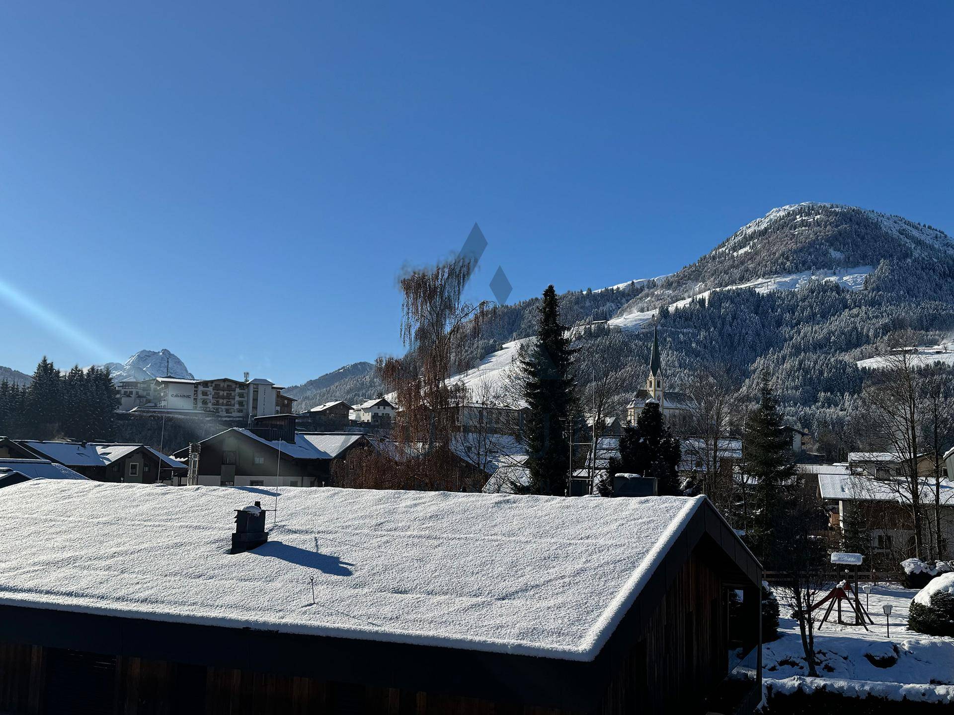Malerische Winterlandschaft mit schneebedeckten Dächern und Bergen unter klarem Himmel.