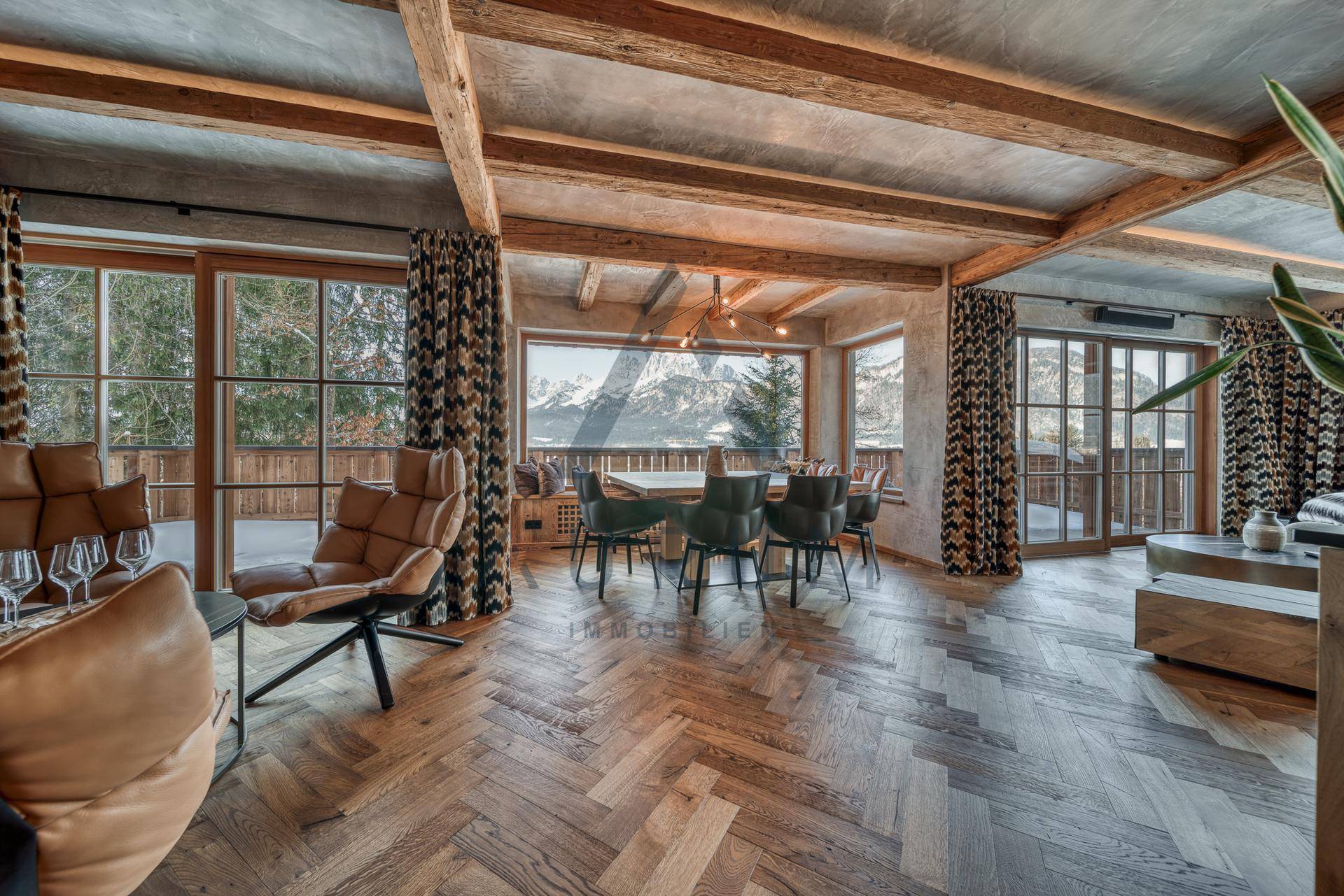 Heller Wohn- und Essbereich mit Fischgrätparkett, Holzbalken und Zugang zu einem Balkon mit Bergblick.