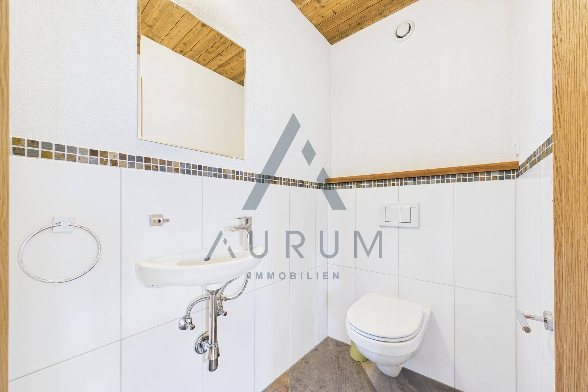 Gäste-WC mit wandhängender Toilette, kleinem Waschbecken und Holzbalkendecke.