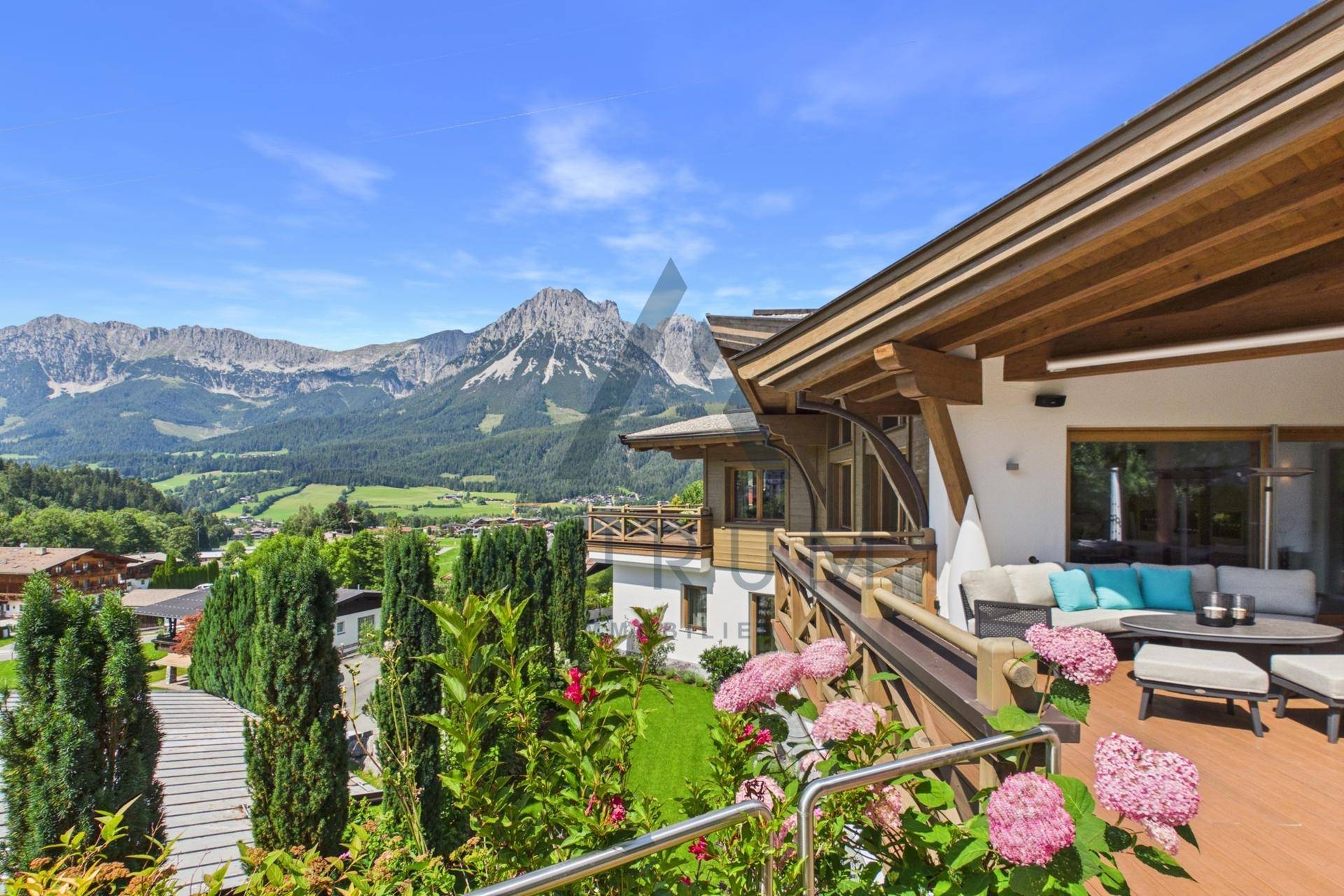 Sonniger Terrassenbereich mit Blumenbeeten und Panoramablick auf die majestätischen Berge.