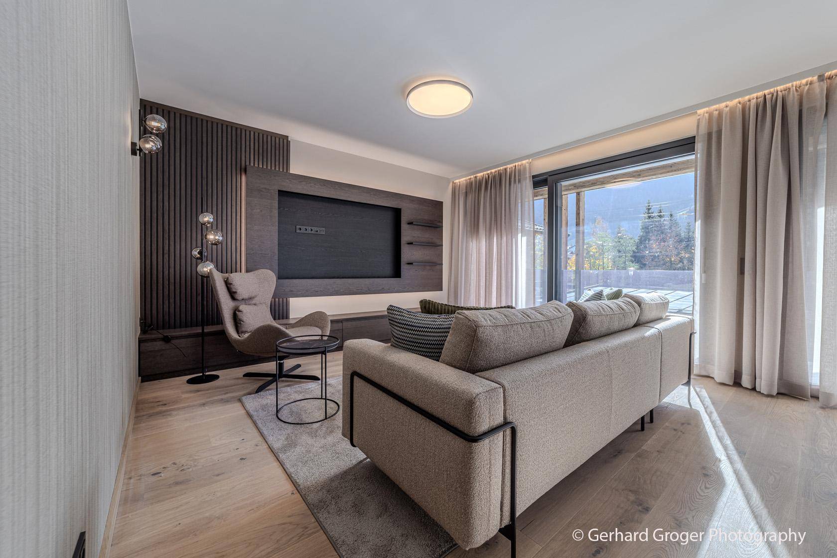 Komfortables Wohnzimmer mit großem Sofa, Holzboden und Zugang zu einem Außenbereich.