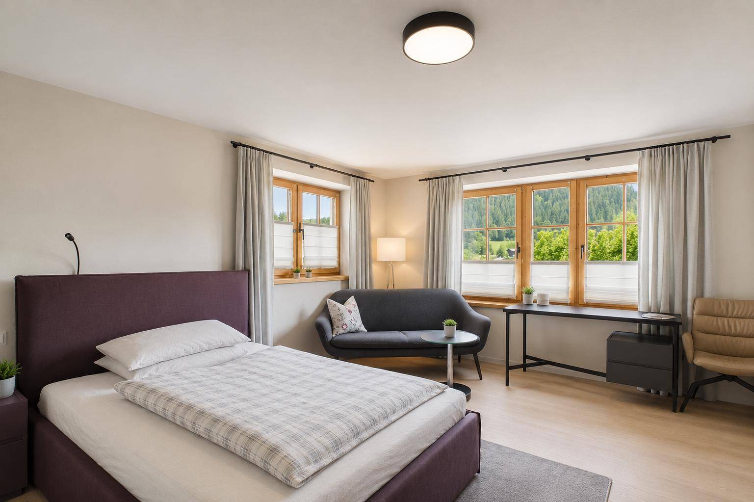 Gemütliches Schlafzimmer mit Einzelbett, Sofa und Fenstern mit Blick ins Grüne.