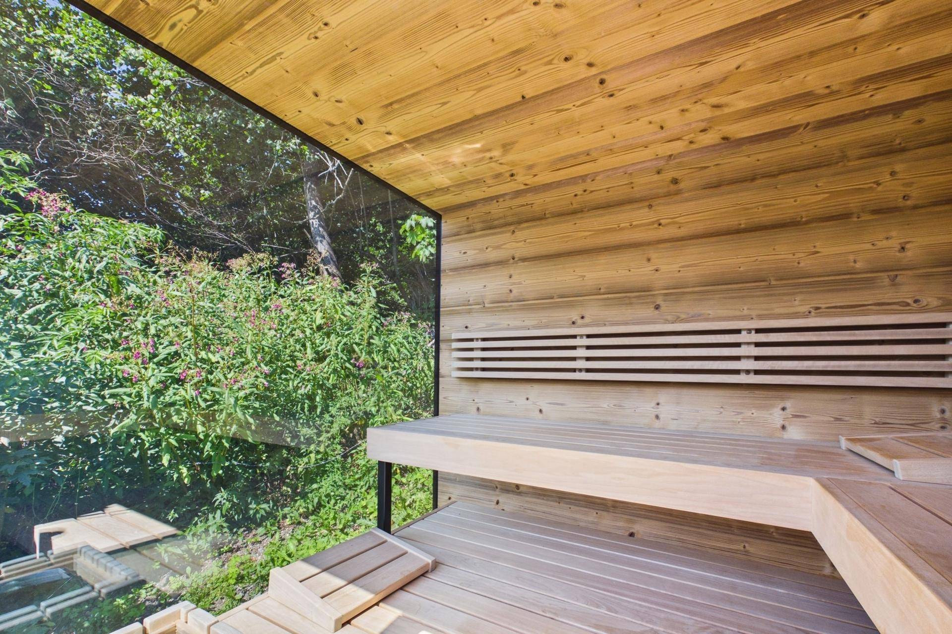 Moderne Sauna mit Holzverkleidung und großer Glasfront mit Blick ins Grüne.