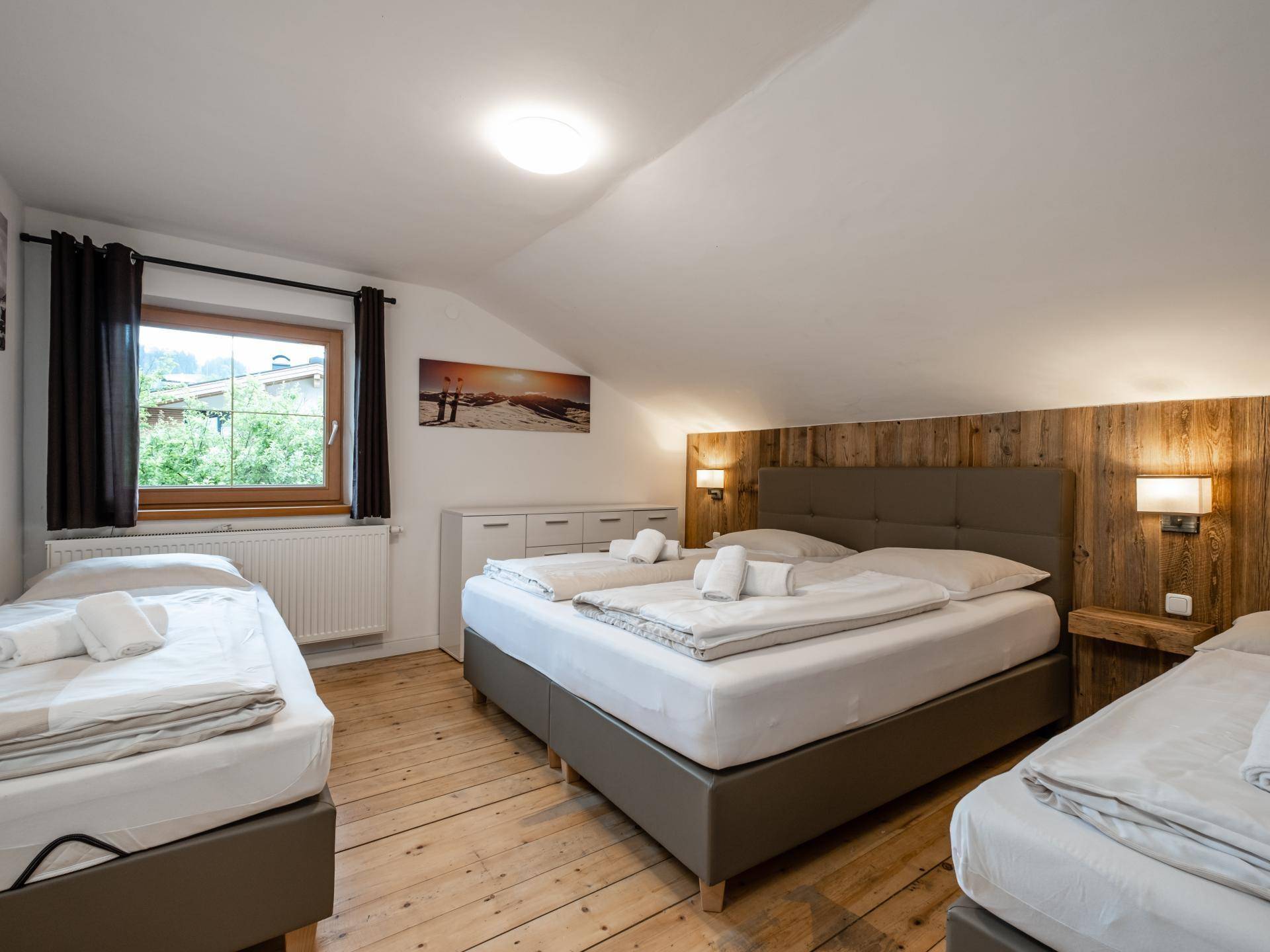 Geräumiges Schlafzimmer mit drei Betten, Dielenboden und Dachschräge, bietet Blick ins Grüne.