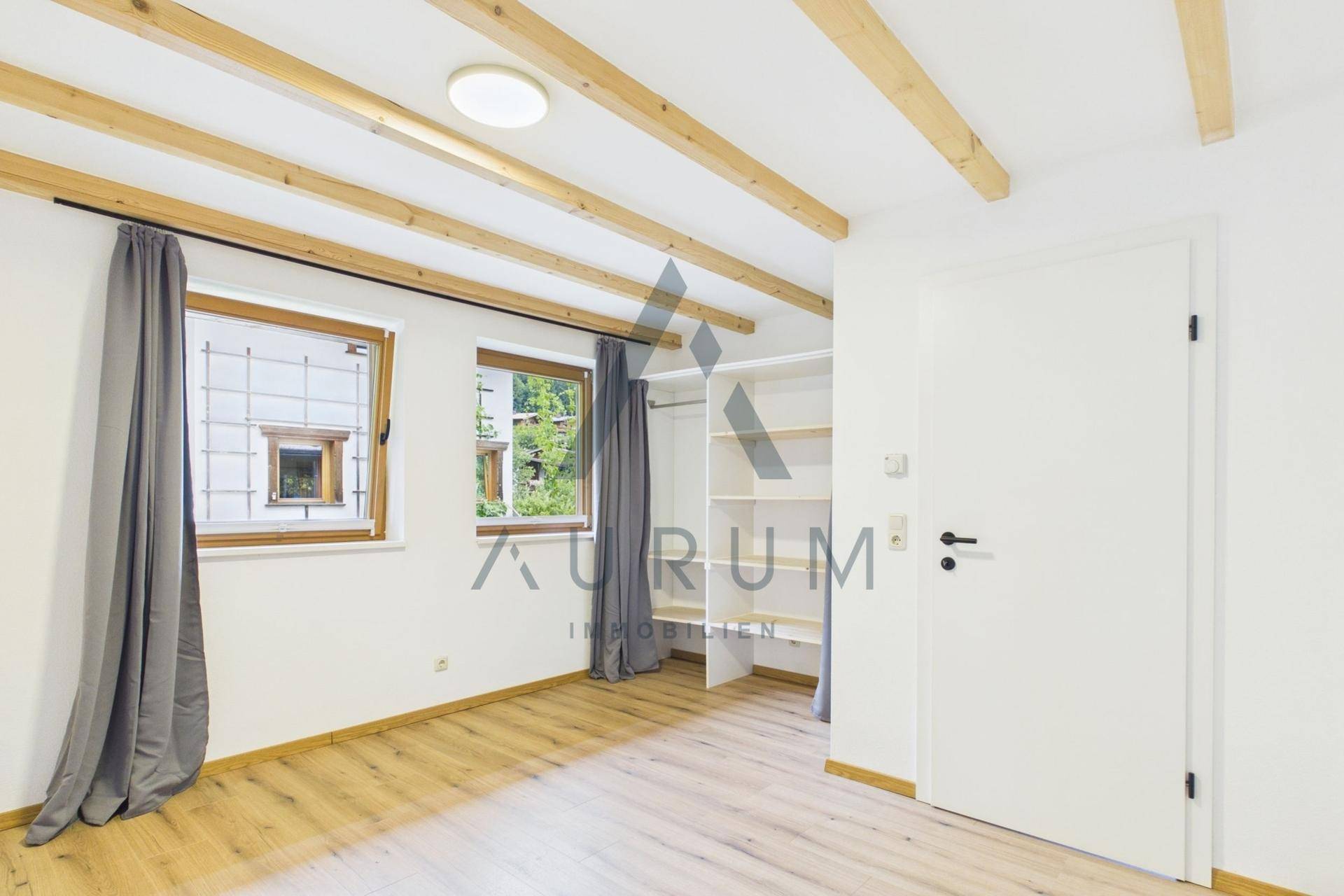 Schlafzimmer mit Holzbalken, Parkettboden und offenem Kleiderschrank.