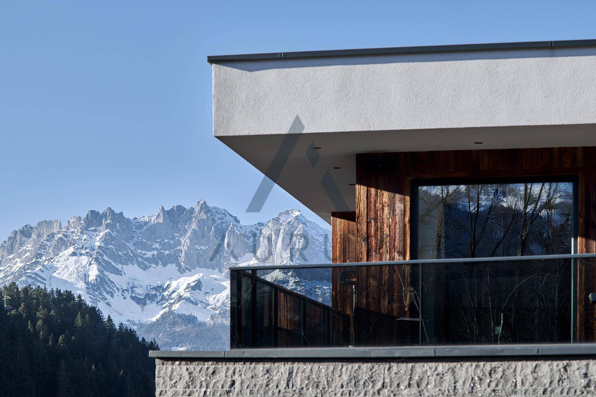 Moderner Balkon mit Glasgeländer und weitem Blick auf die schneebedeckten Berge unter blauem Himmel.