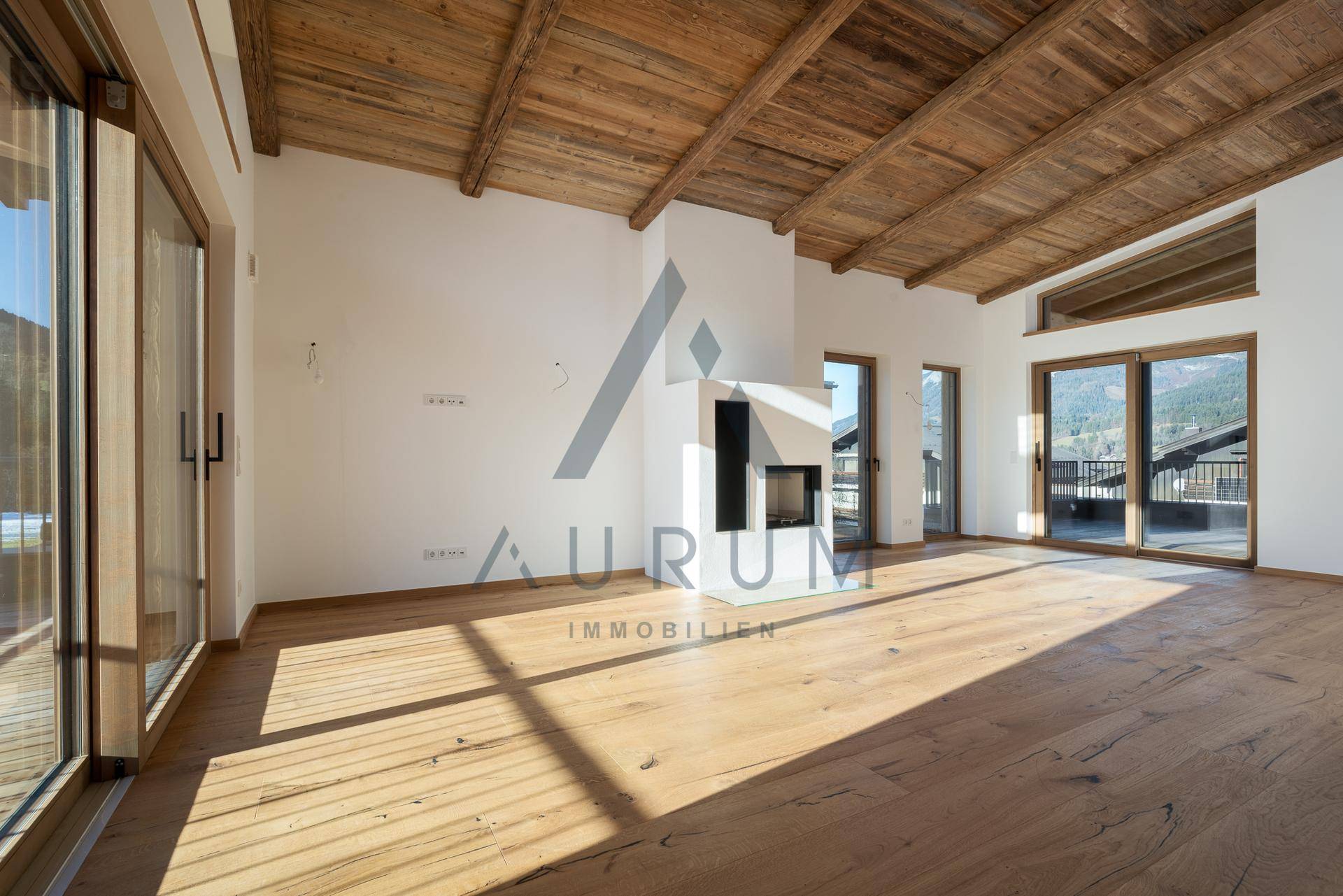 Heller Wohnraum mit Holzboden, sichtbaren Holzbalken und einem eleganten Kamin als Mittelpunkt.