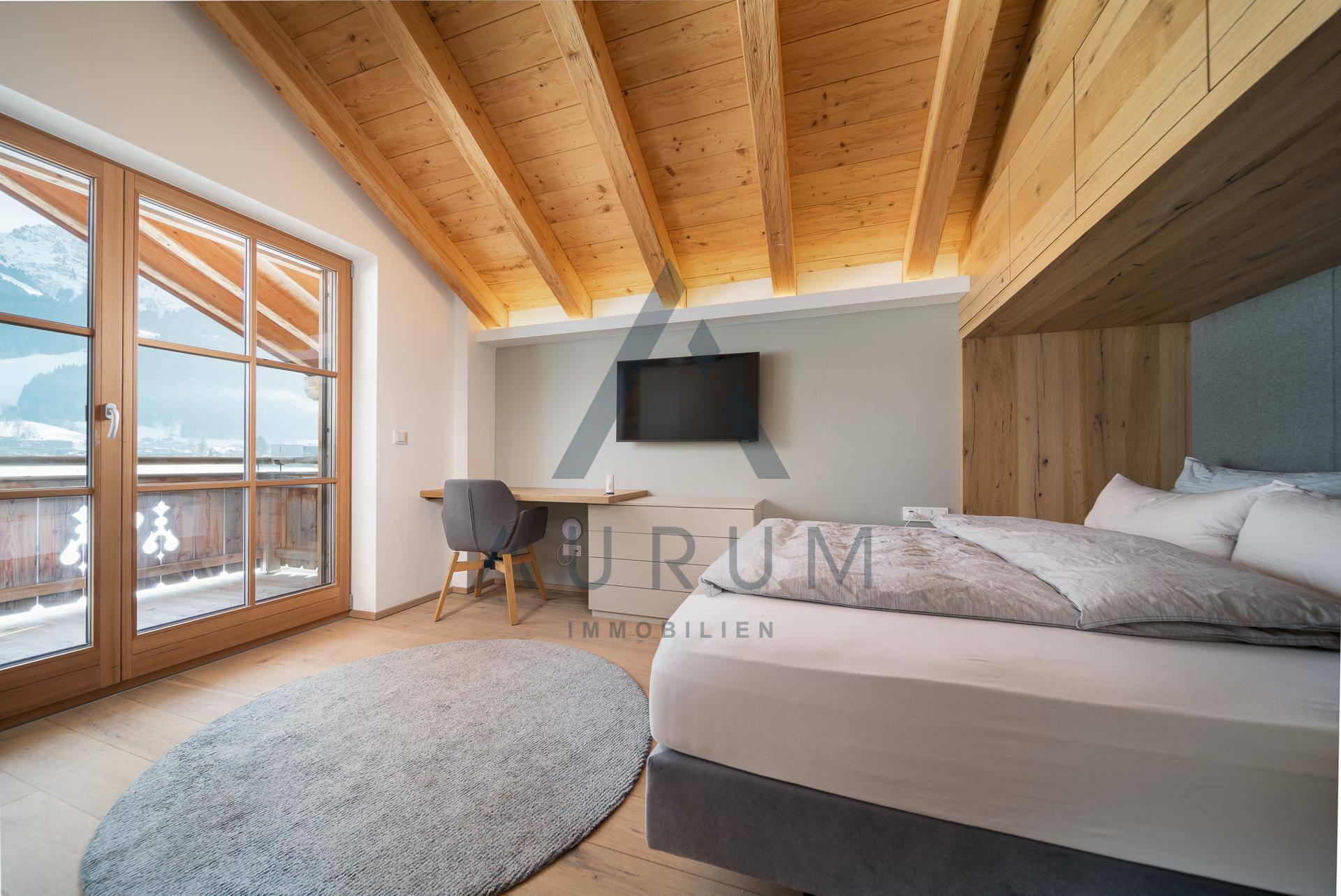 Helles Schlafzimmer mit Holzbalkendecke, Schreibtisch und Bergblick vom Balkon.
