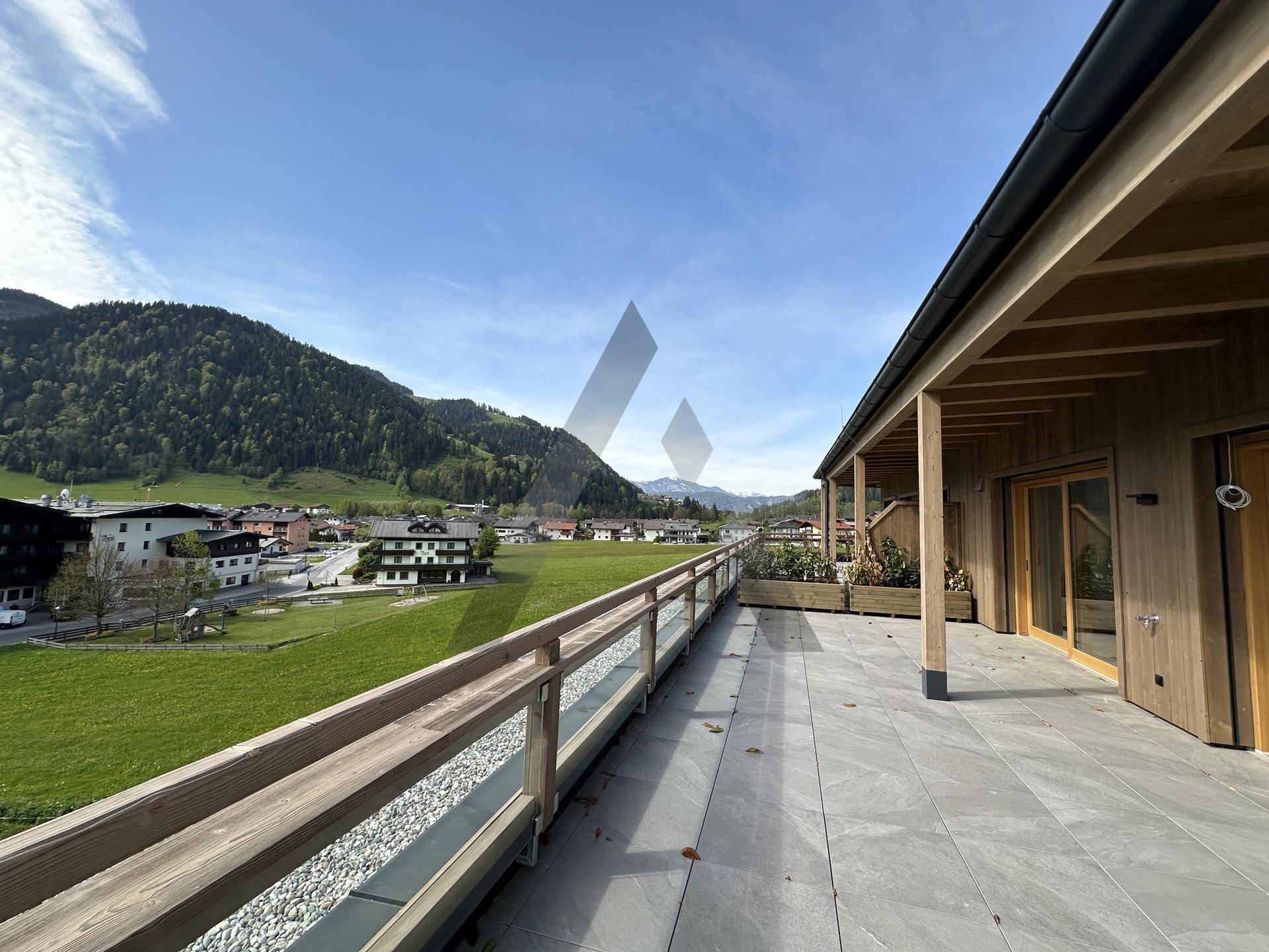 Geräumige Dachterrasse mit Fliesenboden, Holzgeländer und weitem Blick auf die Berglandschaft.