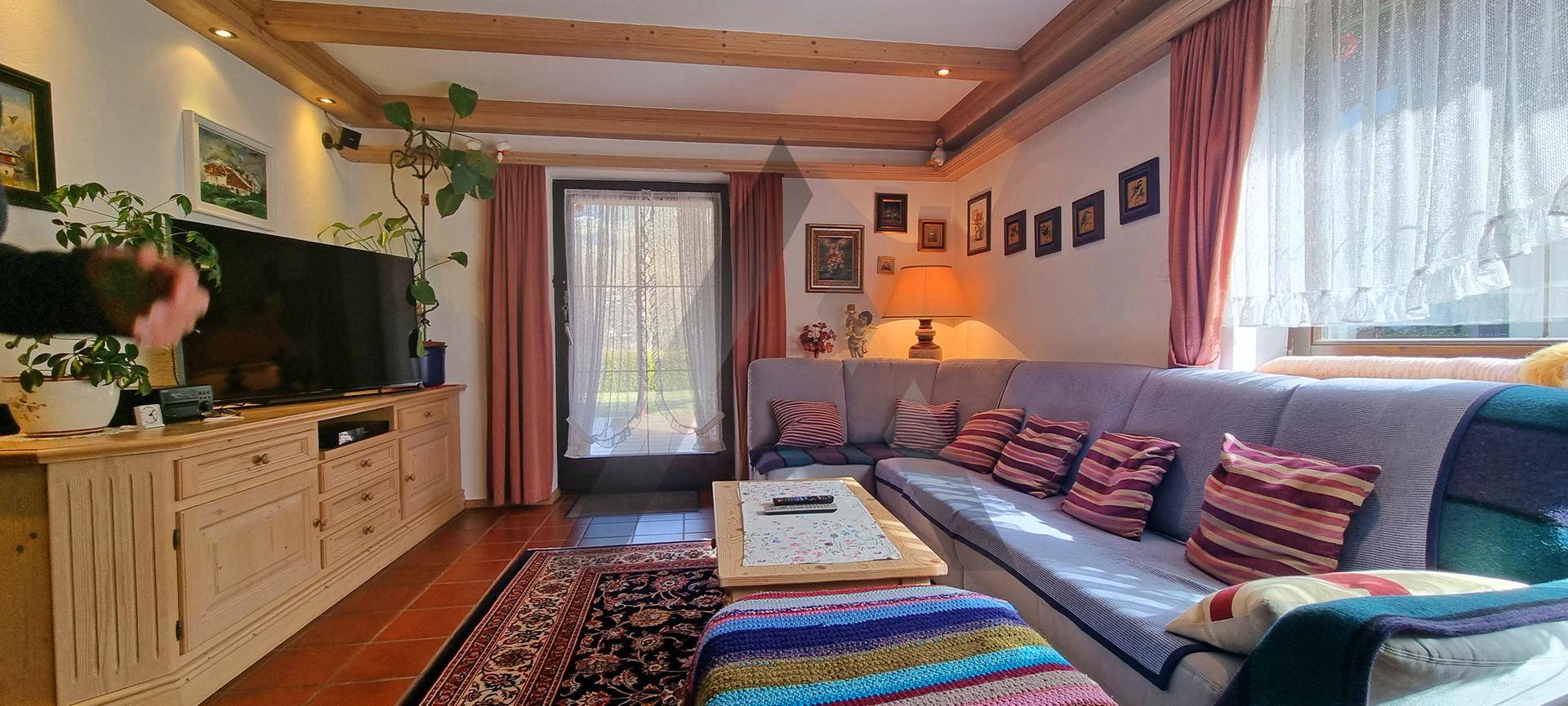 Helles und gemütliches Wohnzimmer mit großem Sofa, Fernseher und sichtbaren Holzbalken an der Decke.