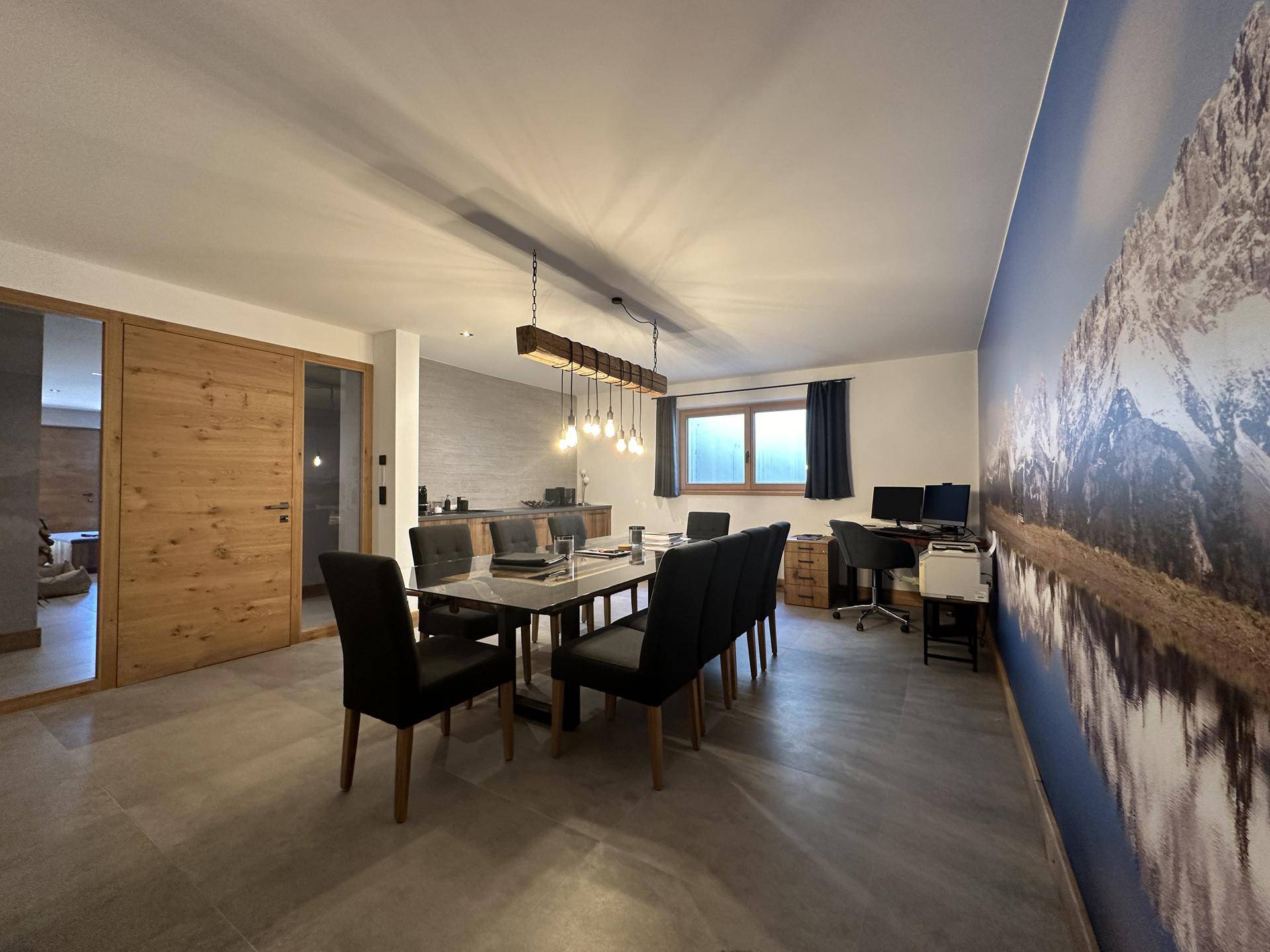 Esszimmer mit großem Tisch, Wandtapete mit Bergmotiv und angrenzendem Arbeitsbereich.