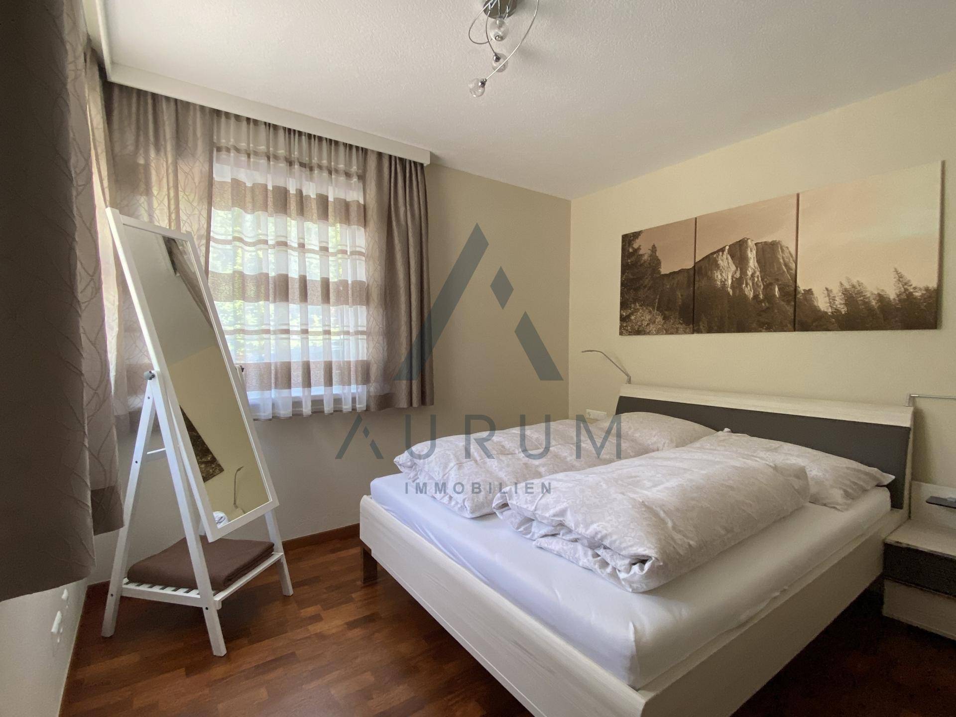Gemütliches Schlafzimmer mit Doppelbett, Holzboden und Fenster mit Vorhängen.