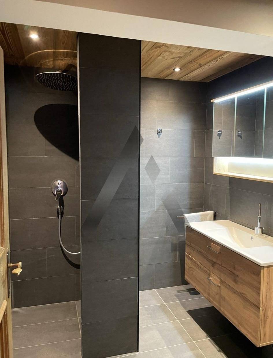 Modernes Badezimmer mit dunklen Fliesen, Holzwaschtisch und großer Regendusche.