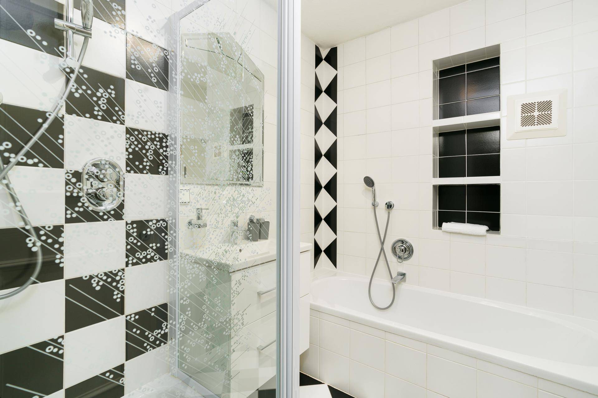 Helles Badezimmer mit Badewanne, Duschkabine und auffälligen schwarz-weißen Fliesen.