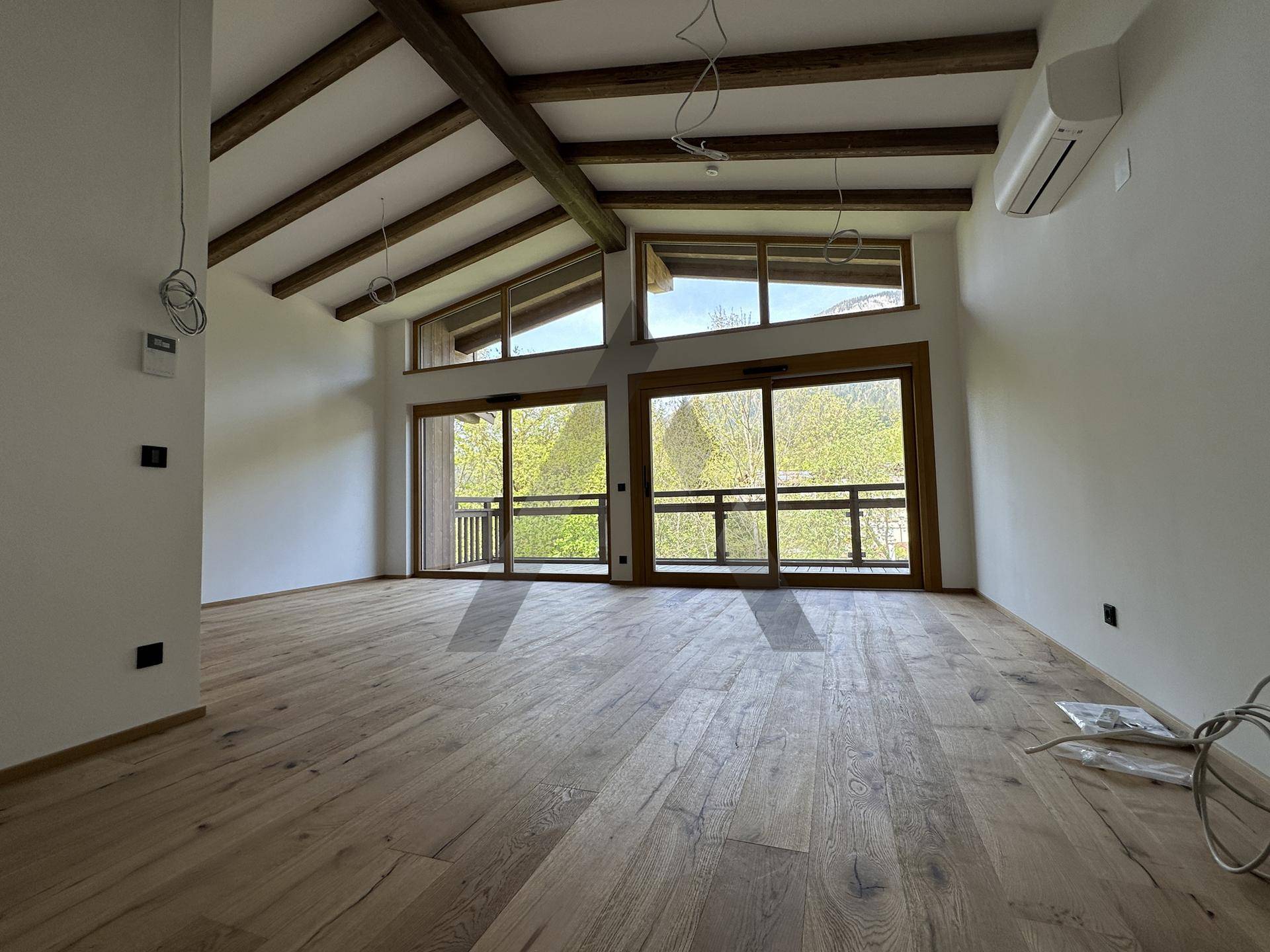Geräumiges Wohnzimmer mit hohen Decken, Holzbalken und großen Fenstern mit Bergblick.