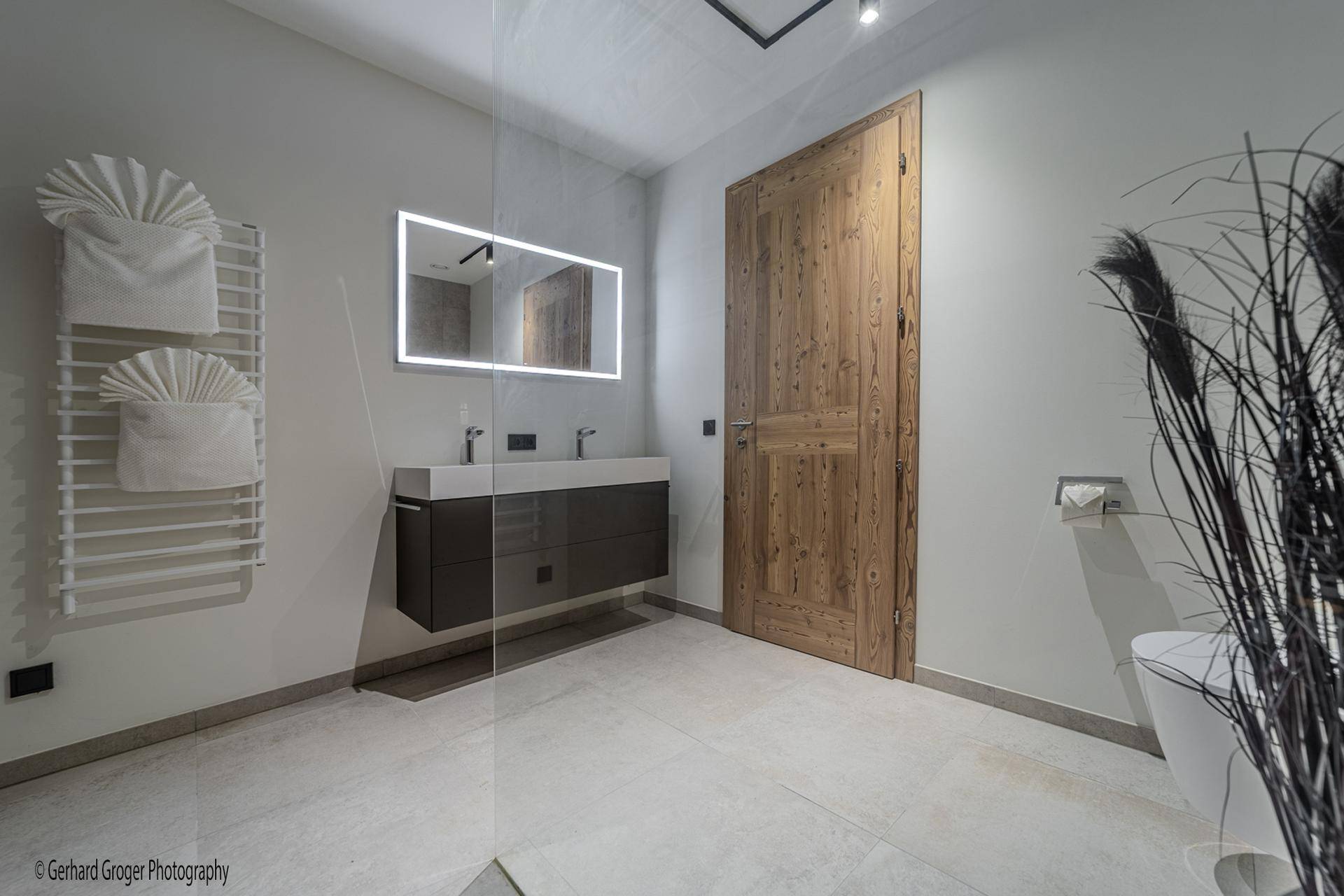 Modernes Badezimmer mit Doppelwaschbecken, beleuchtetem Spiegel und begehbarer Dusche.