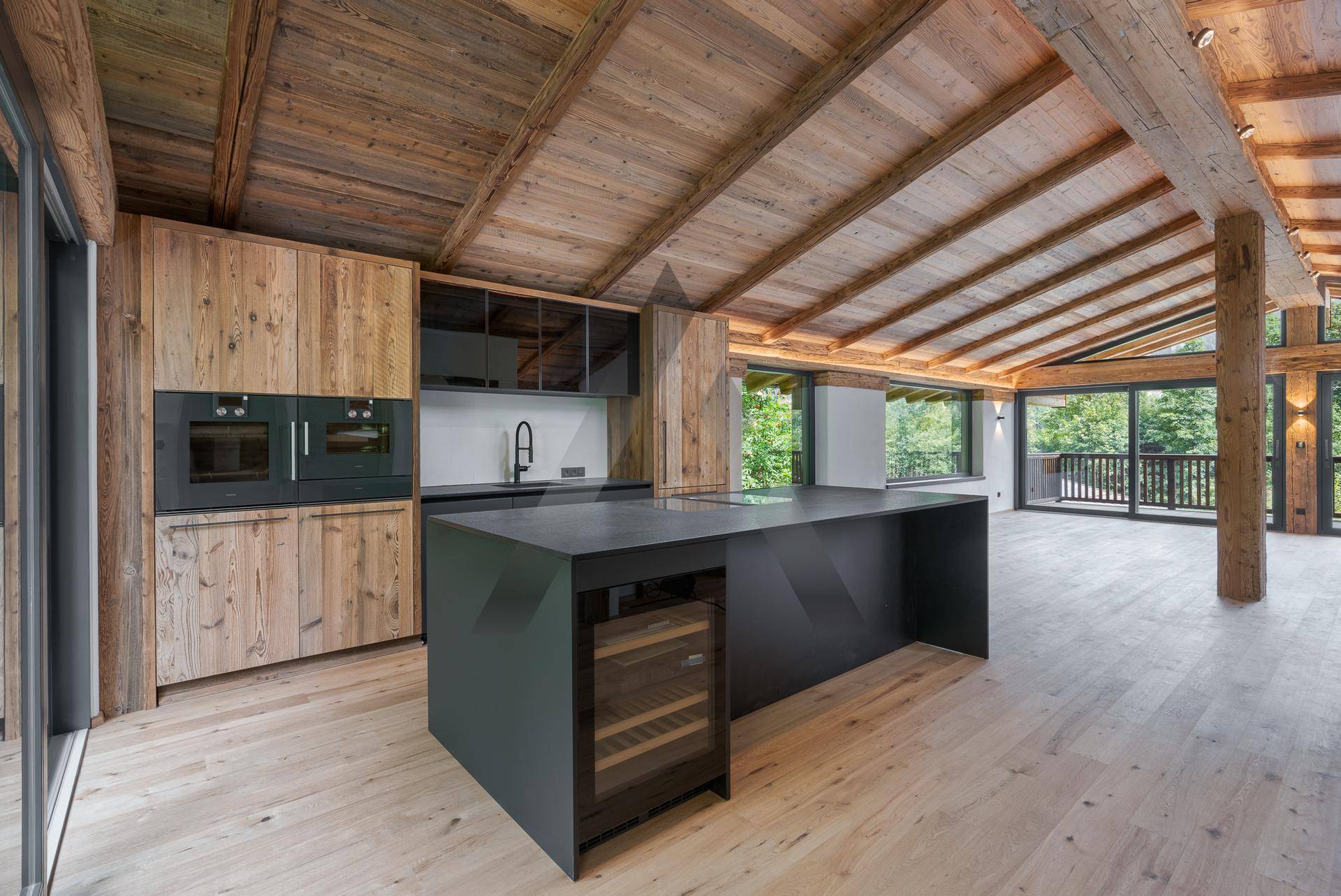Moderne Einbauküche mit dunkler Kücheninsel, Holzschränken und hochwertigen Geräten in offenem Raum.