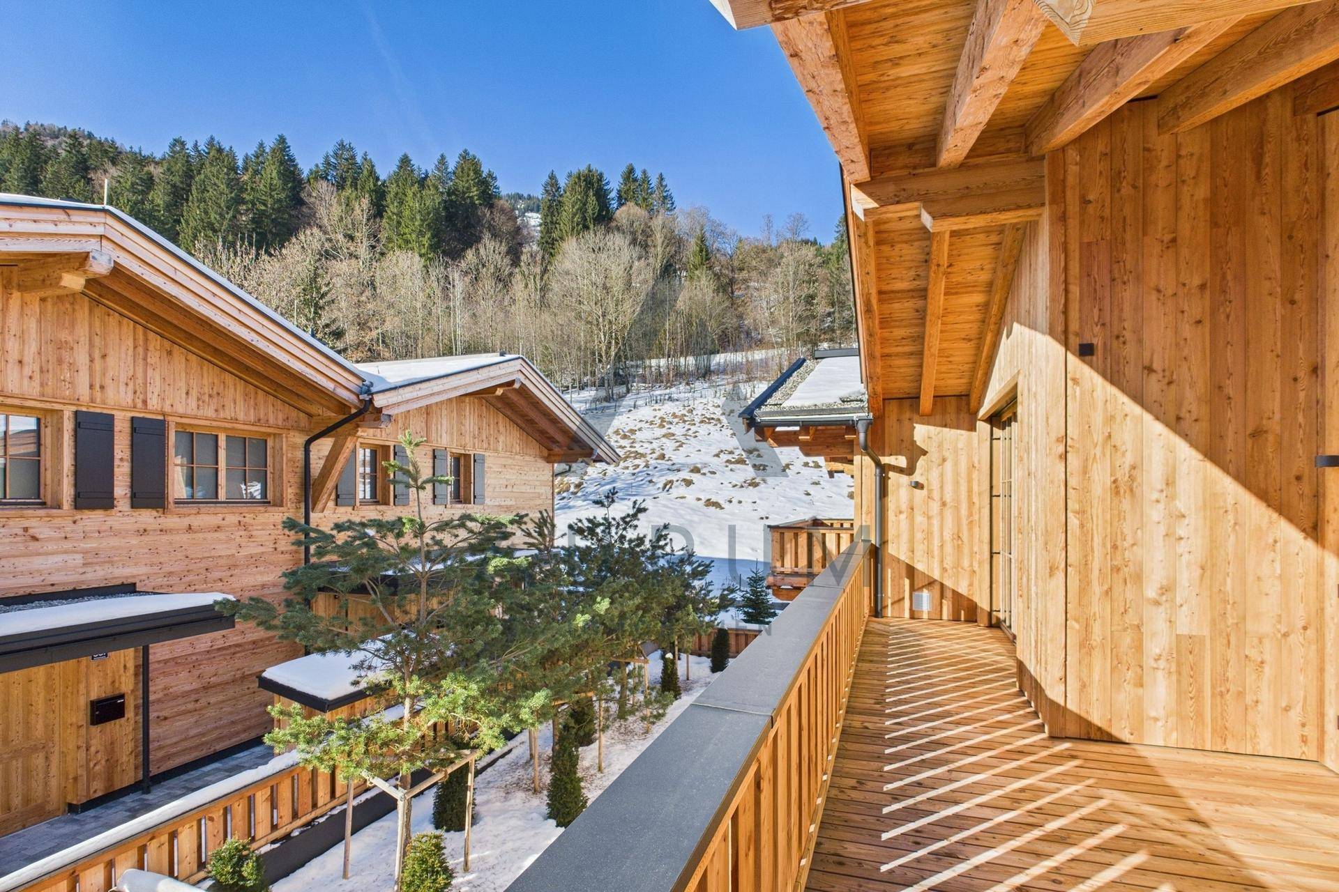 Geräumiger Holzbalkon mit Blick auf andere Chalets und die verschneite Berglandschaft.