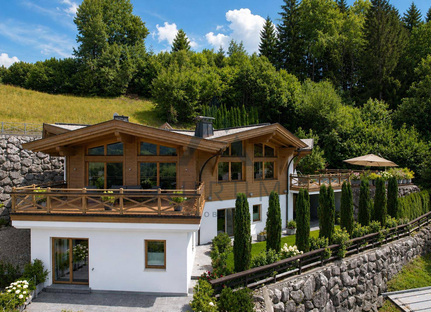 Charmantes Chalet mit Holzfassade und Steinelementen, umgeben von grünen Hügeln und Bäumen.