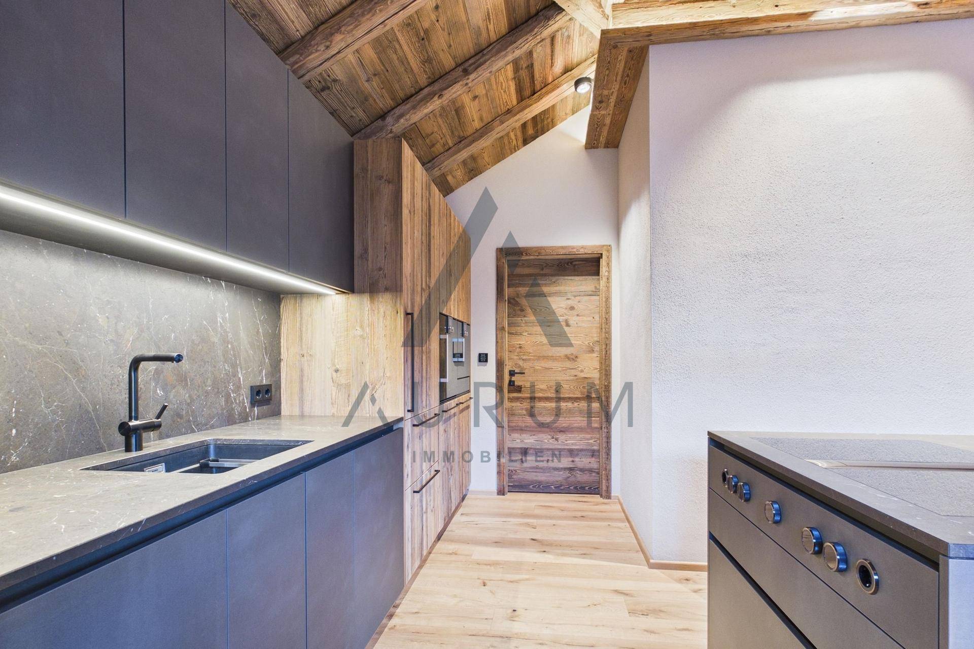 Stilvolle Küche mit dunklen Schränken, Holzelementen, integriertem Backofen und einer Holztür.