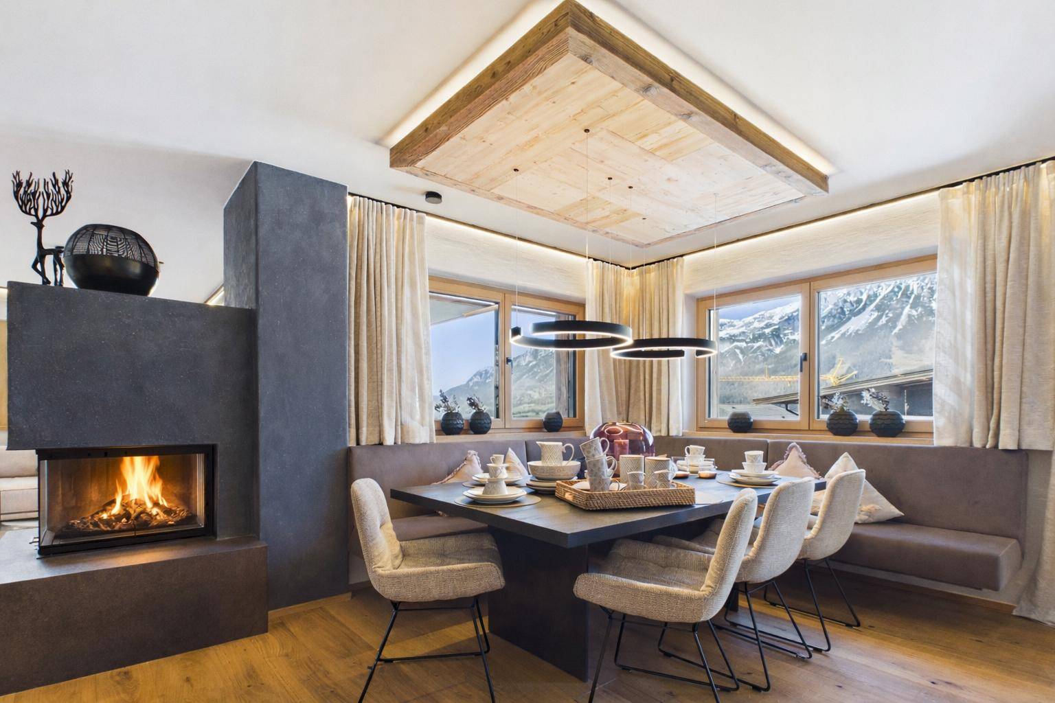 Gemütlicher Essbereich mit Kamin, Holzboden und Bergblick durch große Fenster.