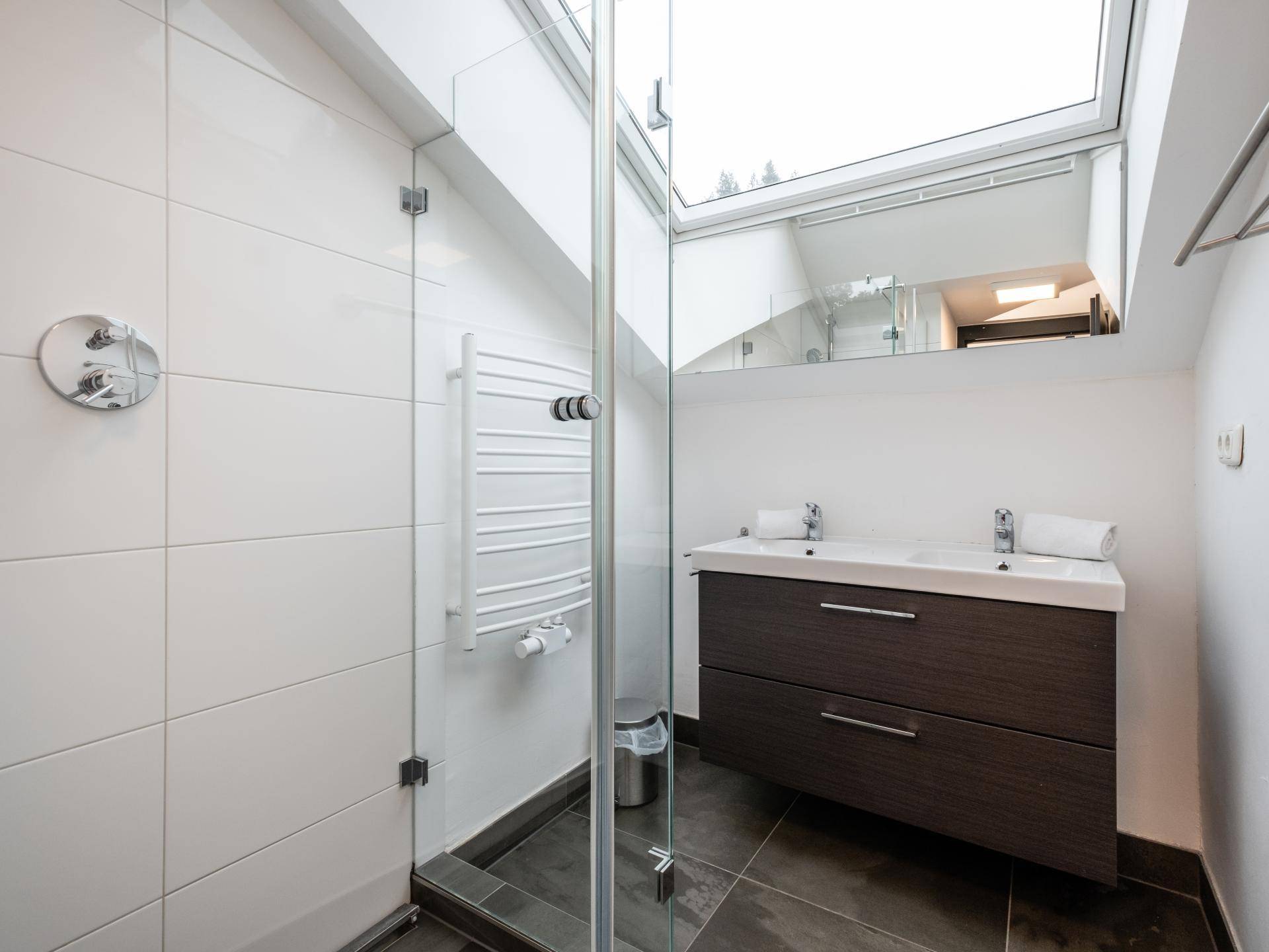 Helles Badezimmer mit ebenerdiger Dusche, Doppelwaschbecken, beheiztem Handtuchhalter und Dachfenster.