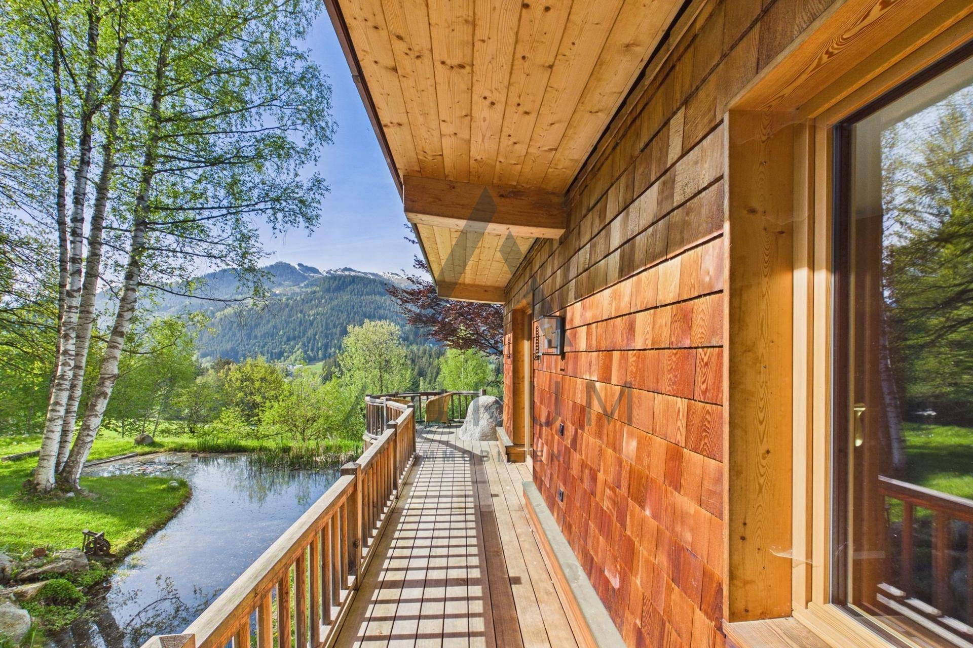 Langer Holzbalkon mit Blick auf den Teich und die umliegende Berglandschaft.