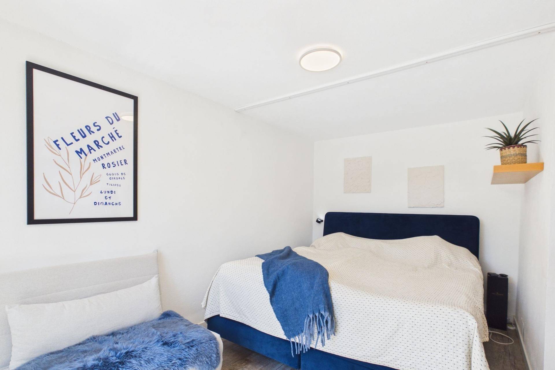 Helles Schlafzimmer mit blauem Bett, weißen Wänden und moderner Dekoration.