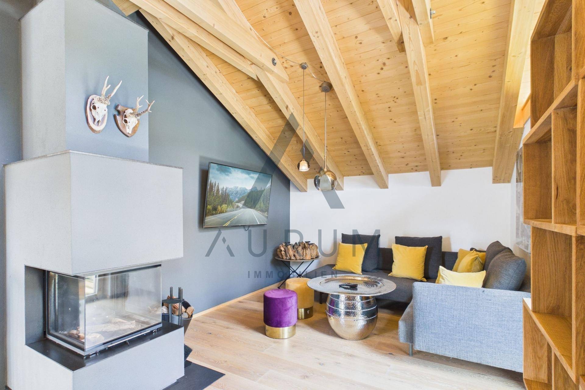 Gemütliches Wohnzimmer mit modernem Kamin, bequemer Couch und Holzbalkendecke.