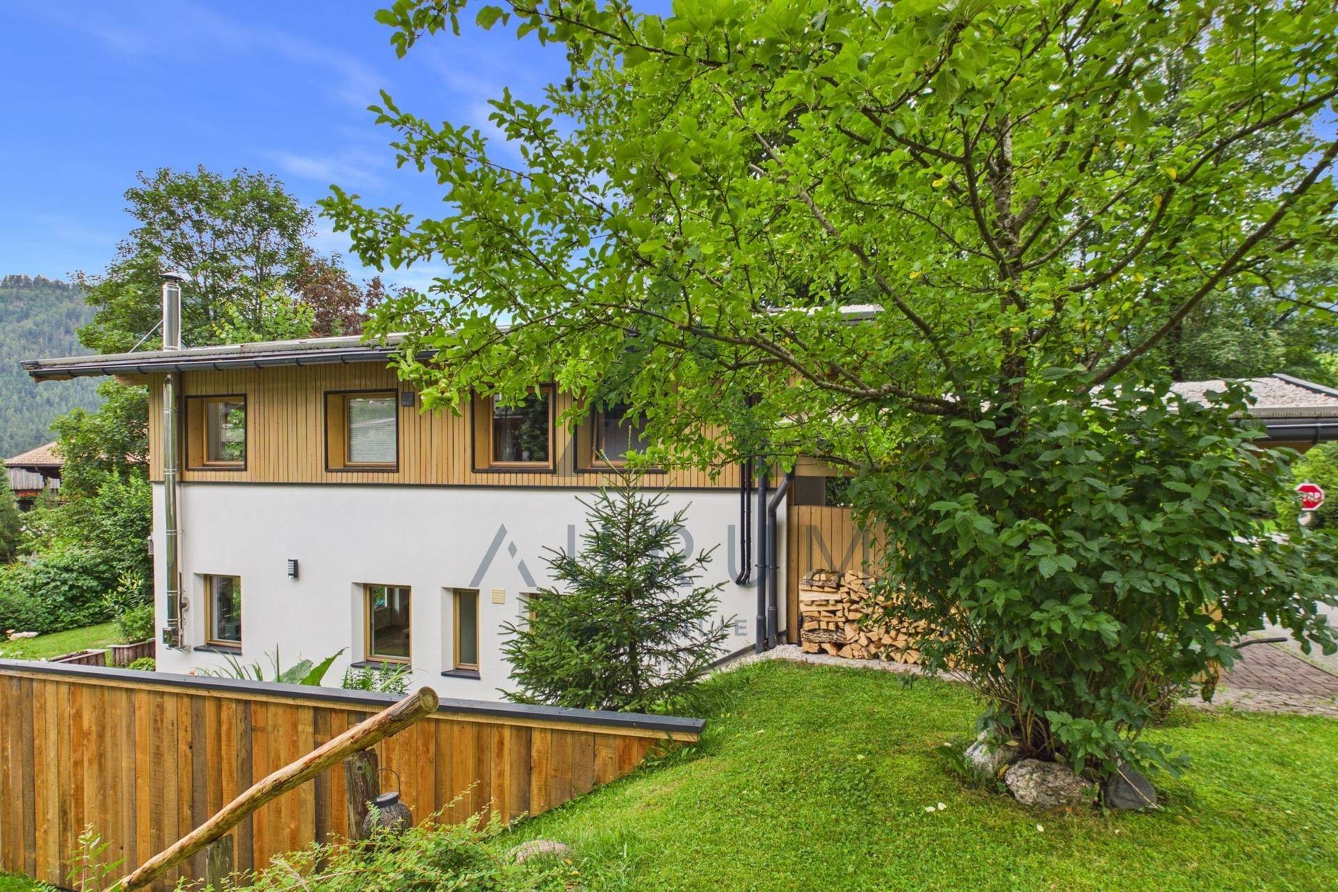 Seitenansicht des Hauses mit Holzfassade und gestapeltem Brennholz.