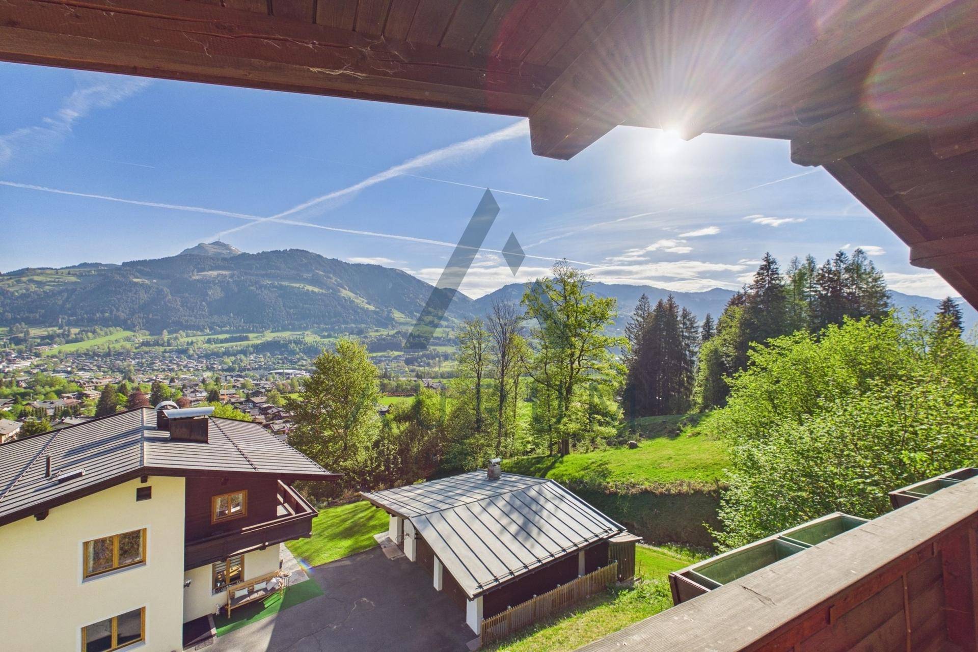 Sonniger Balkonblick über benachbarte Häuser, einen Carport und die beeindruckende Bergkulisse.
