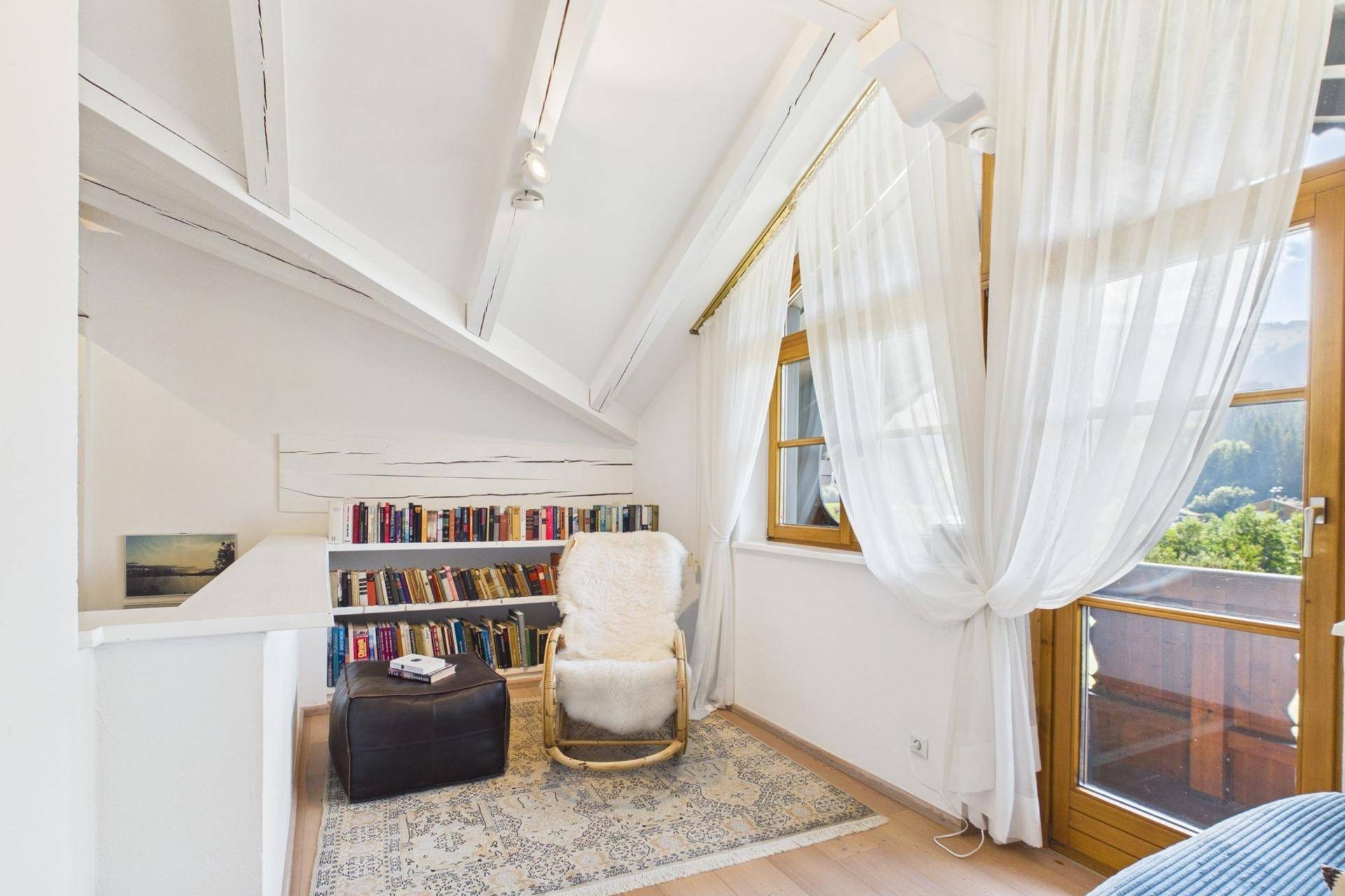 Gemütliche Leseecke im Dachgeschoss mit Bücherregal, bequemen Sessel und Blick ins Grüne.