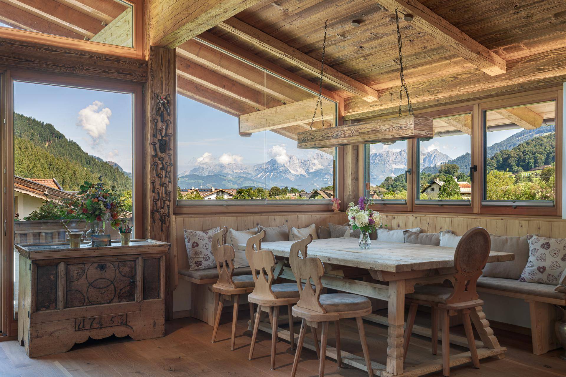 Gemütlicher Essbereich mit Holztisch und Sitzbank, umgeben von großen Fenstern mit Panoramablick auf die Berge.