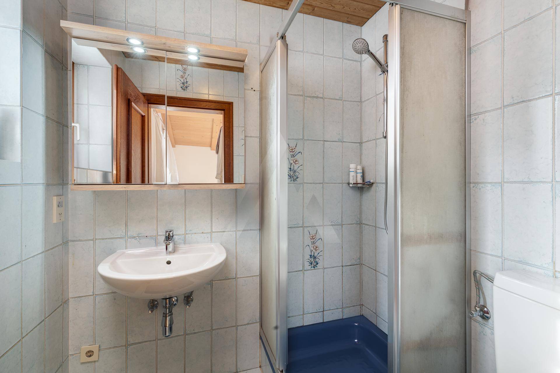 Funktionales Badezimmer mit Duschkabine, Einzelwaschbecken und hellen Fliesen an den Wänden.