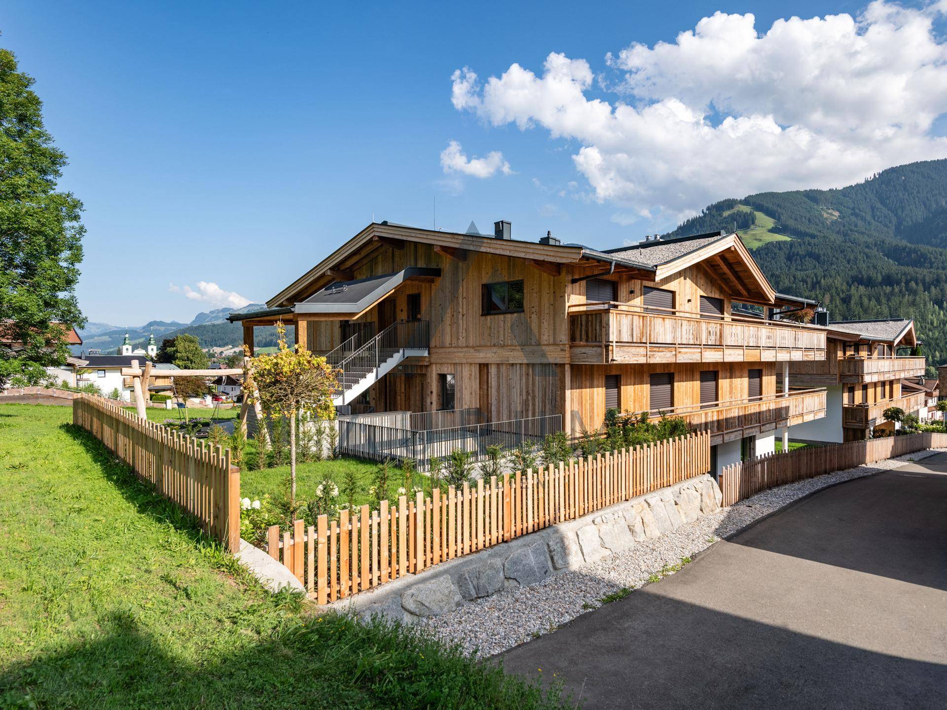Modernes Holzhaus im Chalet-Stil mit mehreren Balkonen, umgeben von grüner Natur und Bergblick.