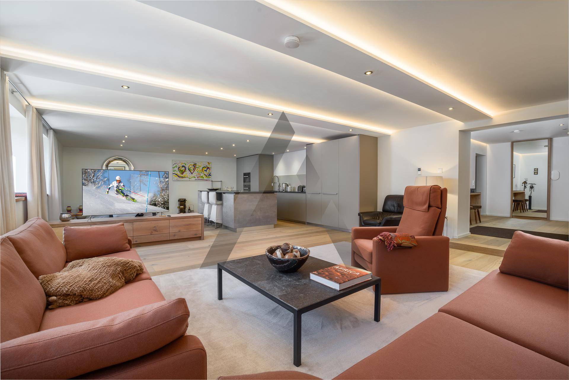 Moderner offener Wohnbereich mit bequemen Sofas, Fernseher und integrierter Küche, ideal für geselliges Beisammensein.