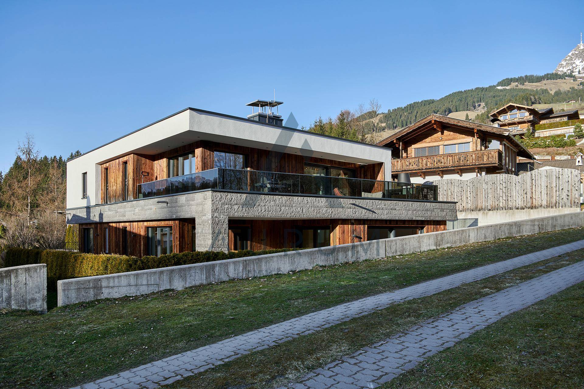 Modernes Wohnhaus mit Holz- und Steinfassade, umgeben von einer gepflegten Auffahrt und Grünflächen.