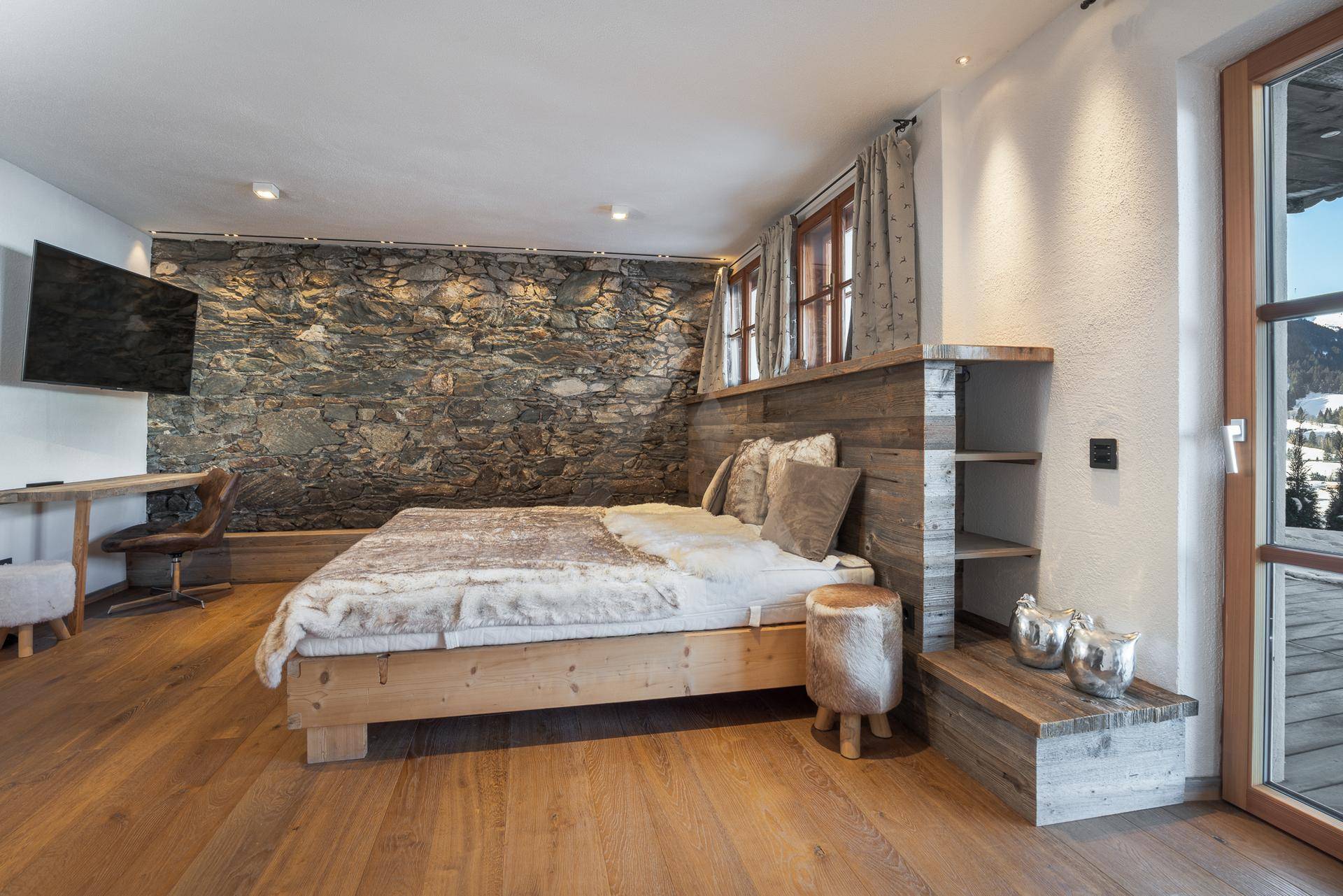 Geräumiges Schlafzimmer mit Steinwand, Holzboden und Blick auf die verschneite Landschaft.