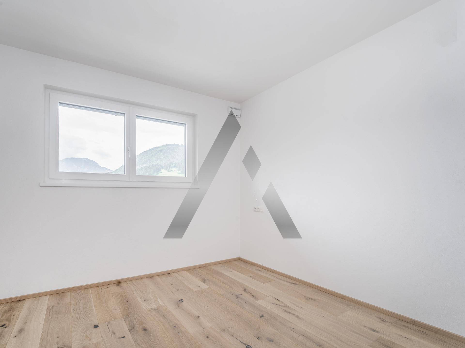 Helles Schlafzimmer mit Holzboden und Fenster, das einen ruhigen Blick auf die grüne Umgebung bietet.
