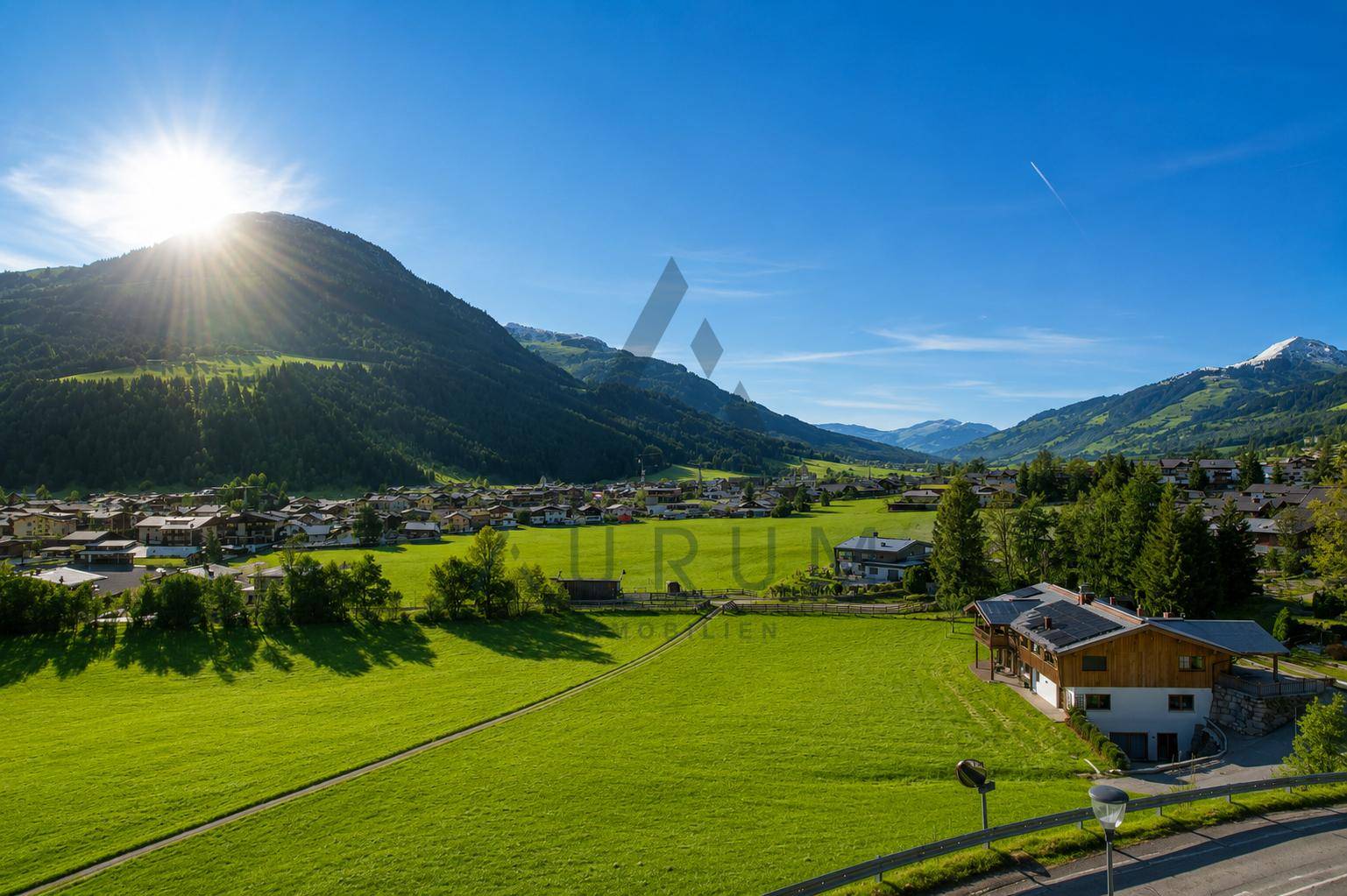 Weitläufiger Ausblick über das Tal mit einem traditionellen Haus im Vordergrund und schneebedeckten Gipfeln in der Ferne.