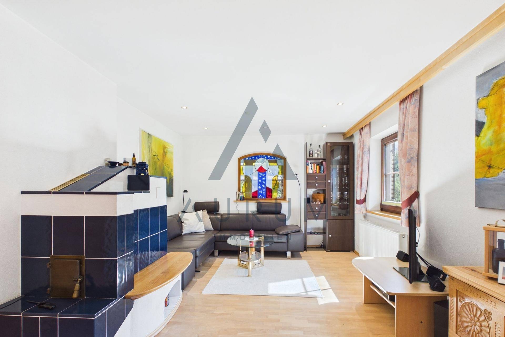 Geräumiges Wohnzimmer mit Kachelofen, Ledersofa und hellem Parkettboden.