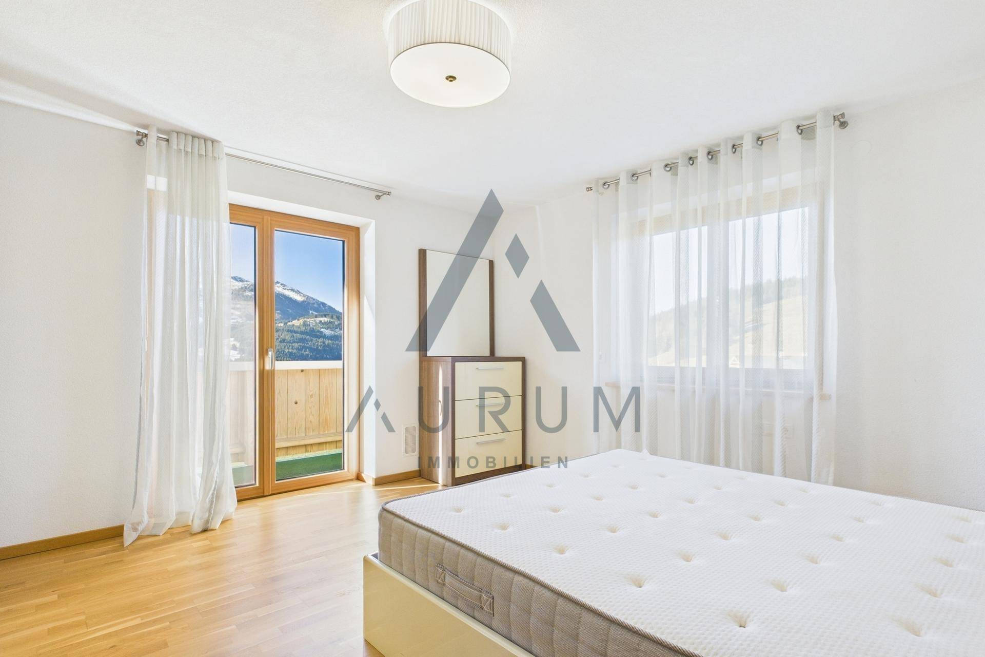 Helles Schlafzimmer mit Holzboden und Zugang zu einem Balkon, der einen weiten Bergblick bietet.