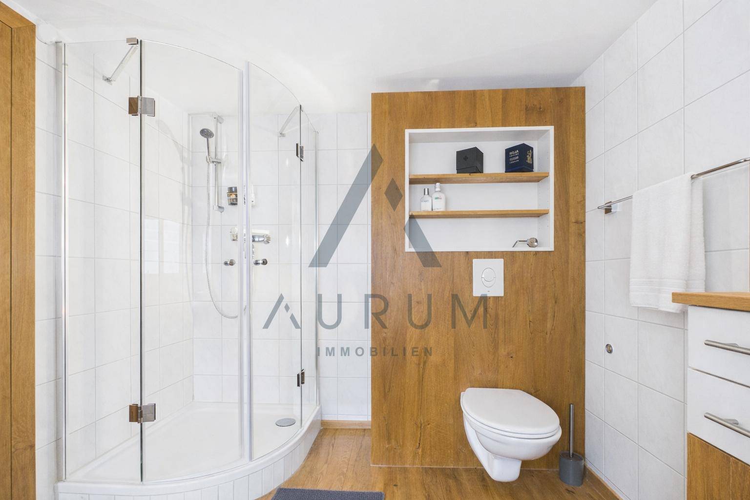 Modernes Badezimmer mit Duschkabine, wandhängendem WC und Holzakzenten.