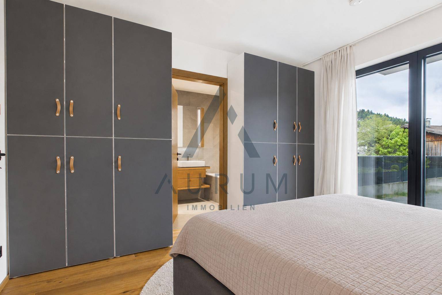 Schlafzimmer mit Einbauschränken und Zugang zu einem modernen Badezimmer sowie zur Terrasse.