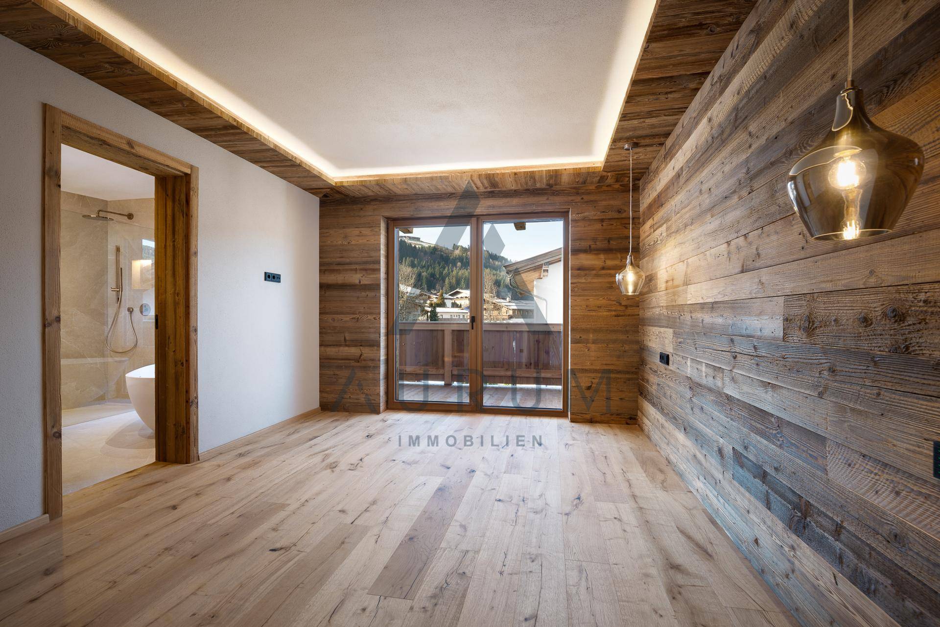 Gemütliches Schlafzimmer mit Holzboden, Holzwänden und Zugang zum Balkon mit Bergblick.