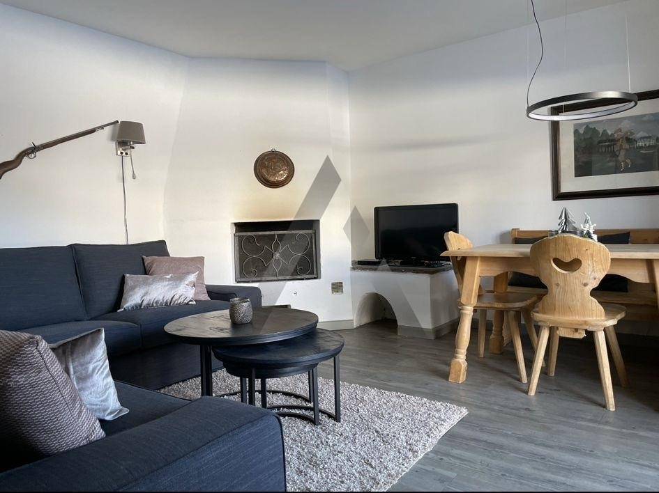 Moderner Wohn-Essbereich mit Kamin, dunklem Sofa und Holztisch.