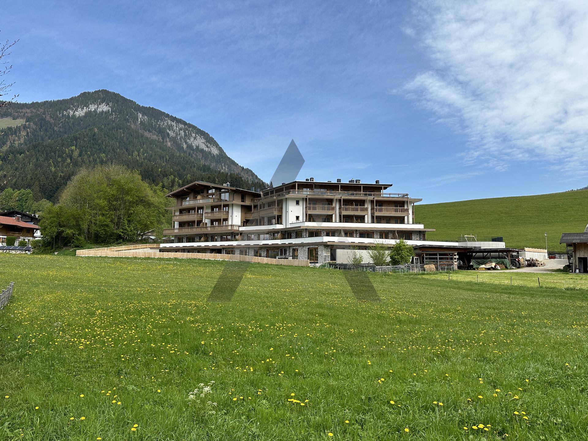 Neues Gebäude in alpiner Landschaft mit grünen Wiesen und Bergen im Hintergrund.